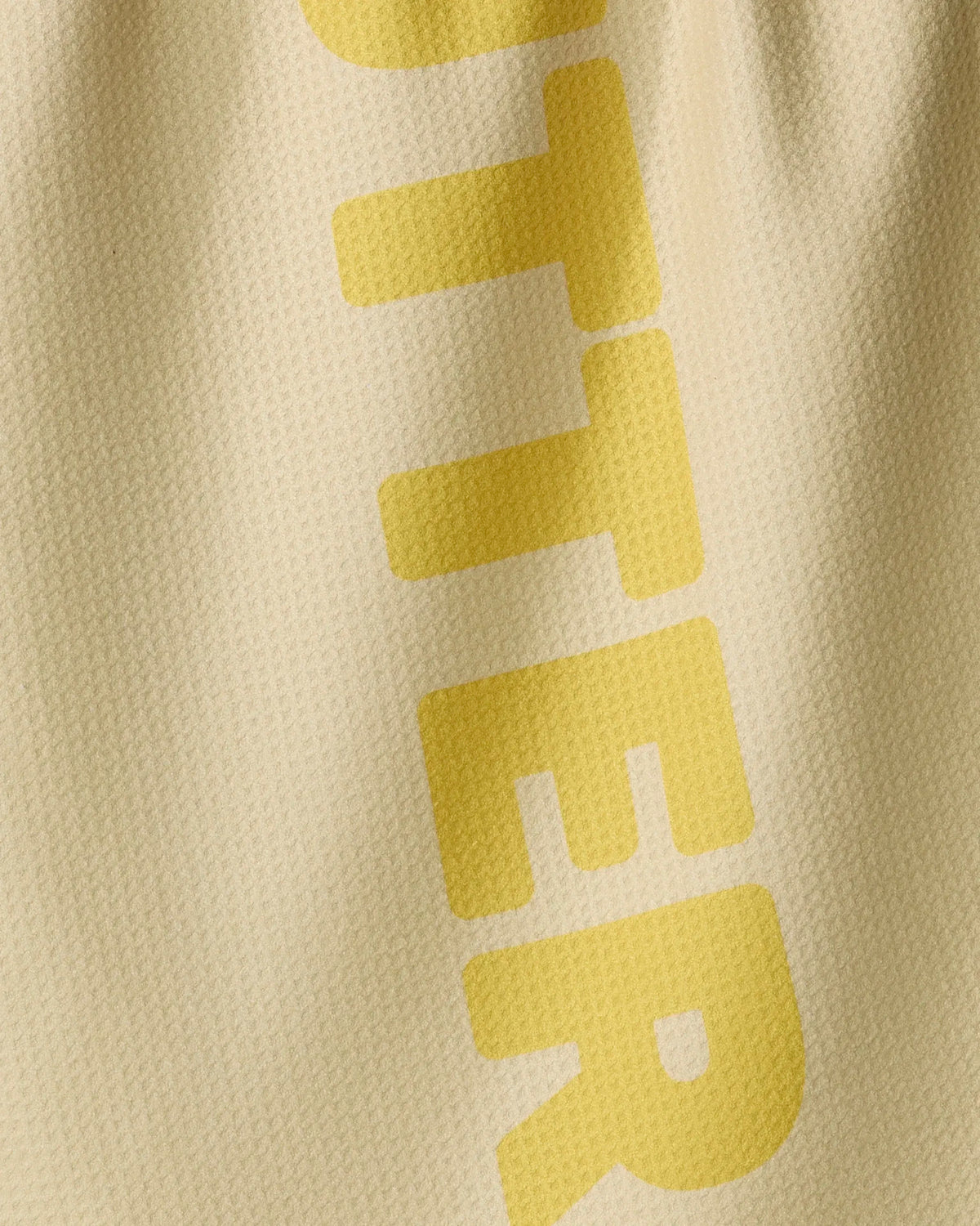 Close-up of a tan recycled GEOMETRY Butter kitchen towel with the yellow letters TTER printed vertically.