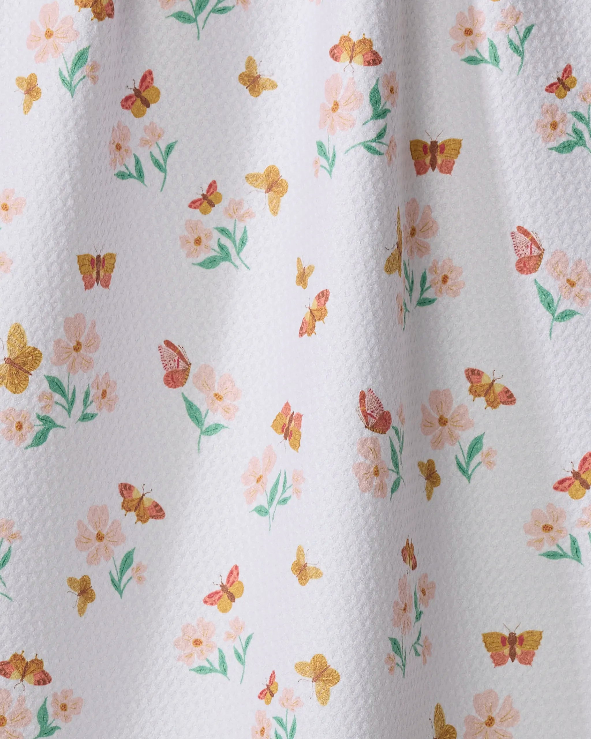 The “Butterfly Garden” kitchen towel by Danelys Sidron is white and textured, decorated with yellow and orange butterflies plus light pink flowers with green stems across the surface.