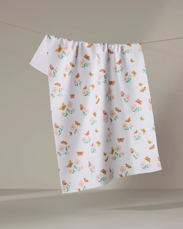 The Danelys Sidron "Butterfly Garden" towel, featuring a white ultra-absorbent textured surface with pastel floral and butterfly patterns, hangs on a clothesline against a plain, light background.