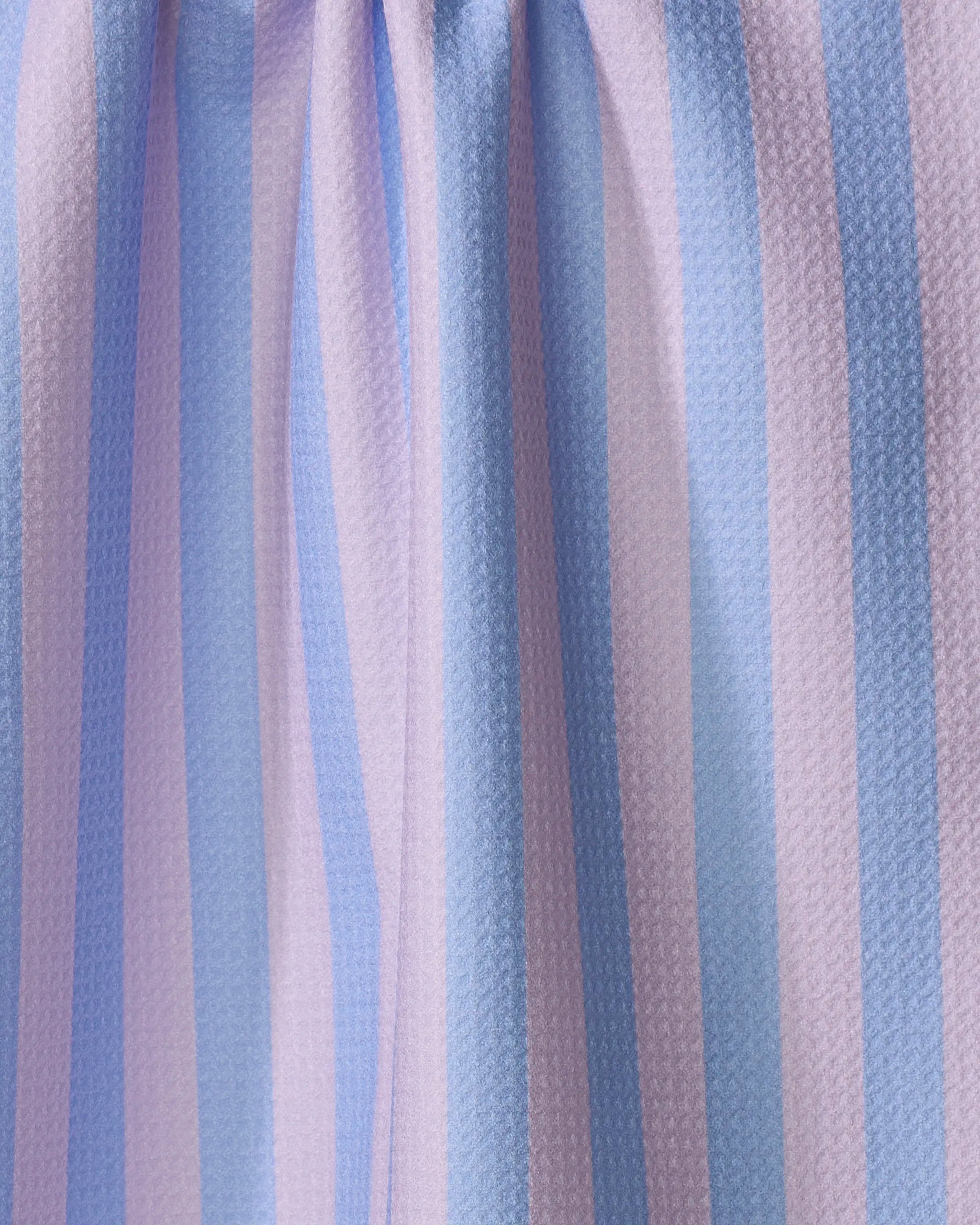 A close-up of The Buy Guide's Cabana Boy - Lilac French Blue tea towel shows vertical pastel stripes in blue, purple, and white on a textured, woven fabric made from quick-drying recycled materials with gentle folds.