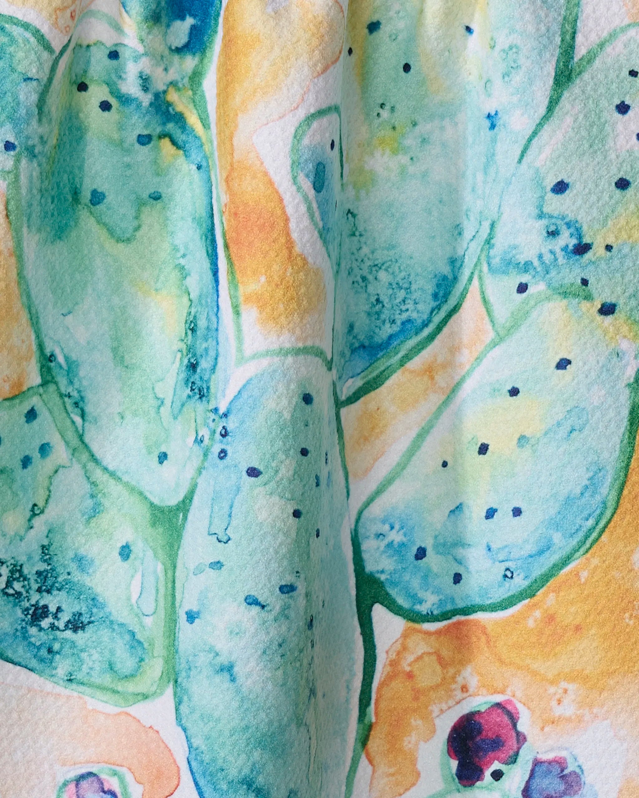 Close-up of Skye Walker's "Cacti" watercolor: green cactus pads with blue outlines and black dots on warm yellow-orange, perfect for adding vibrant color to a quick-dry tea towel made from recycled materials.