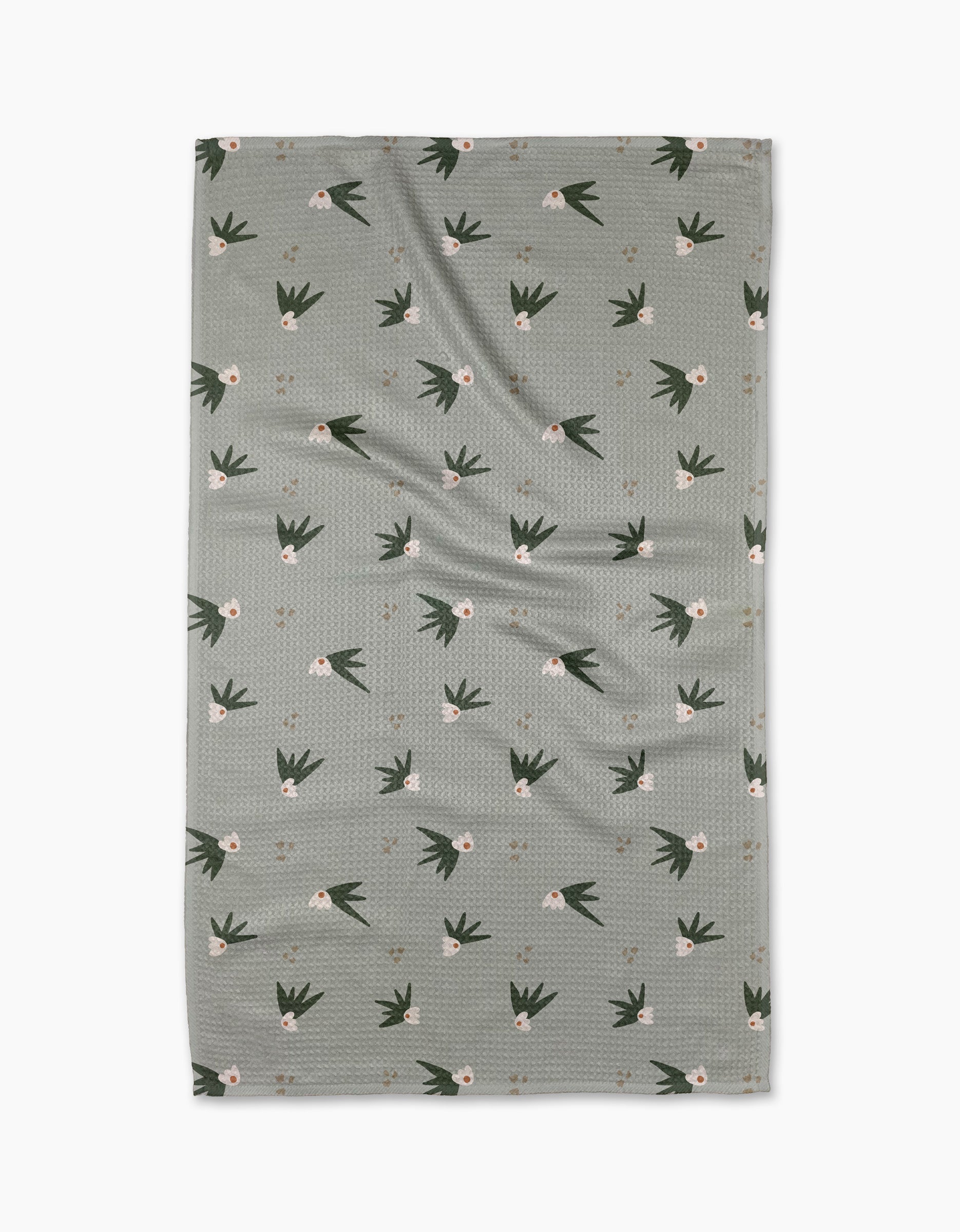 The Cali Sun Agave tea towel by Amberleigh Adoff features a grayish-green rectangular design with a subtle texture, scattered white flowers, and dark green leaves, expertly crafted from recycled materials.