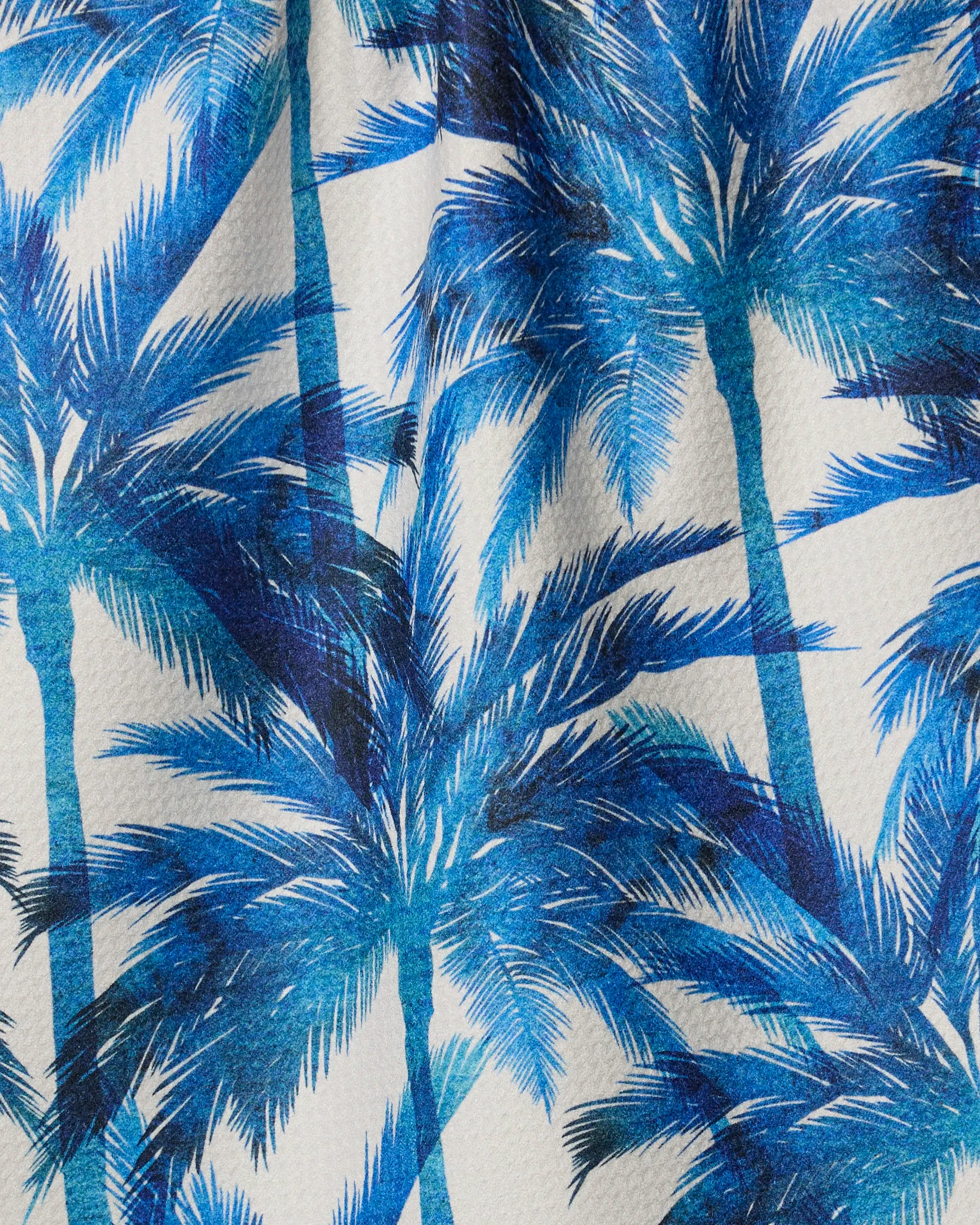 Caligo by Geometry features blue palm tree silhouettes with layered fronds on white textured fabric, creating a tropical, summery look—ideal for a kitchen tea towel made from recycled materials.
