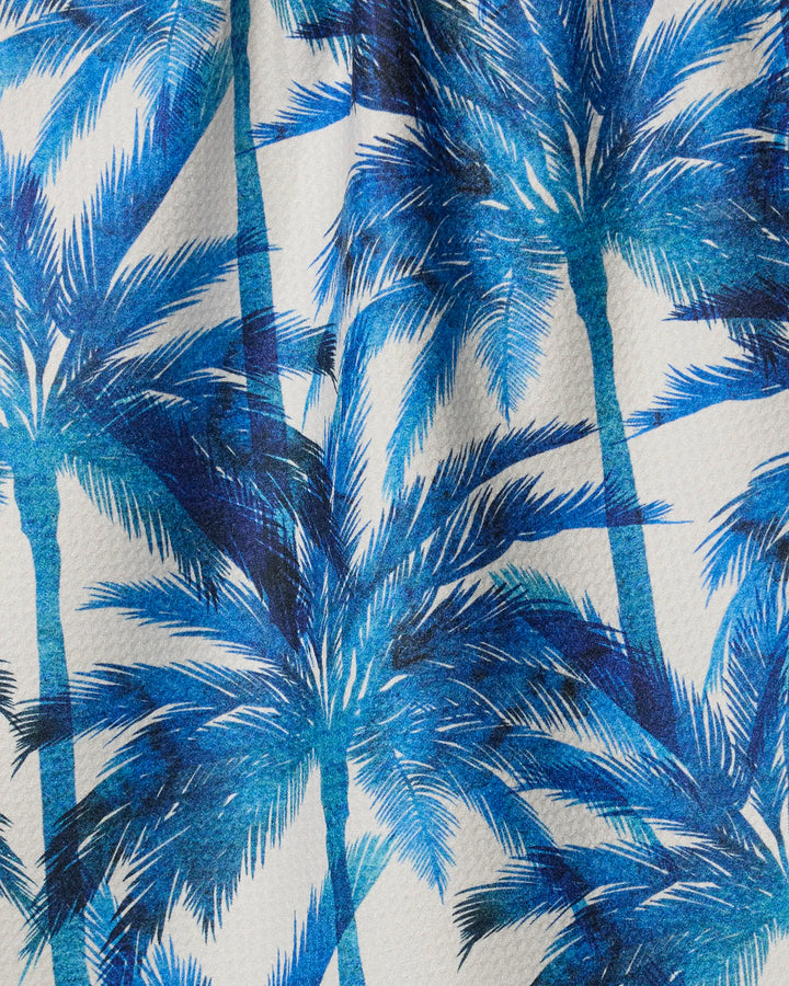 Caligo by Geometry features blue palm tree silhouettes with layered fronds on white textured fabric, creating a tropical, summery look—ideal for a kitchen tea towel made from recycled materials.