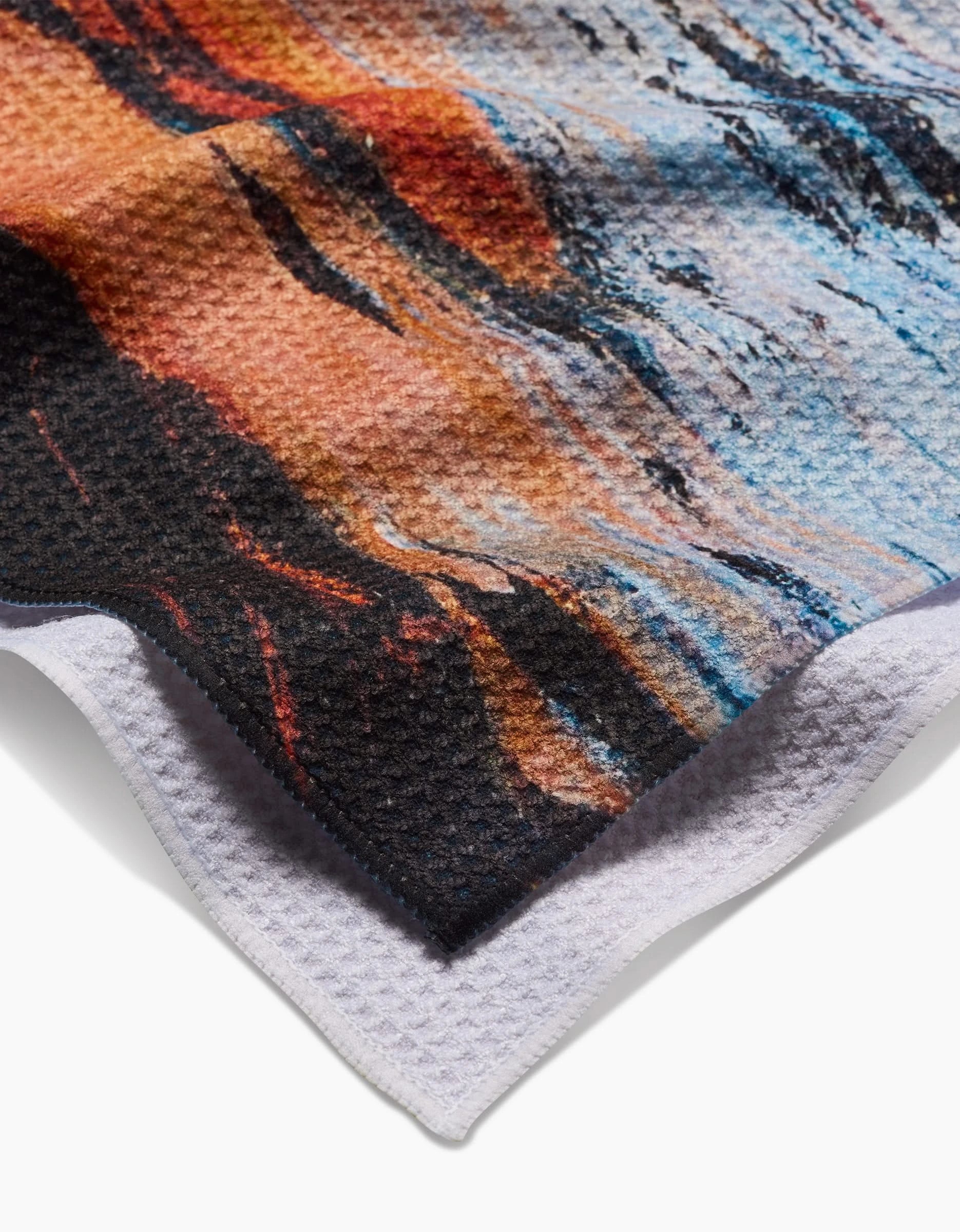 A close-up of Stefanie Bales Call Of The Wild Tea Towel, made from recycled materials, showcases a colorful abstract earth-toned pattern with blue accents and a white edge.