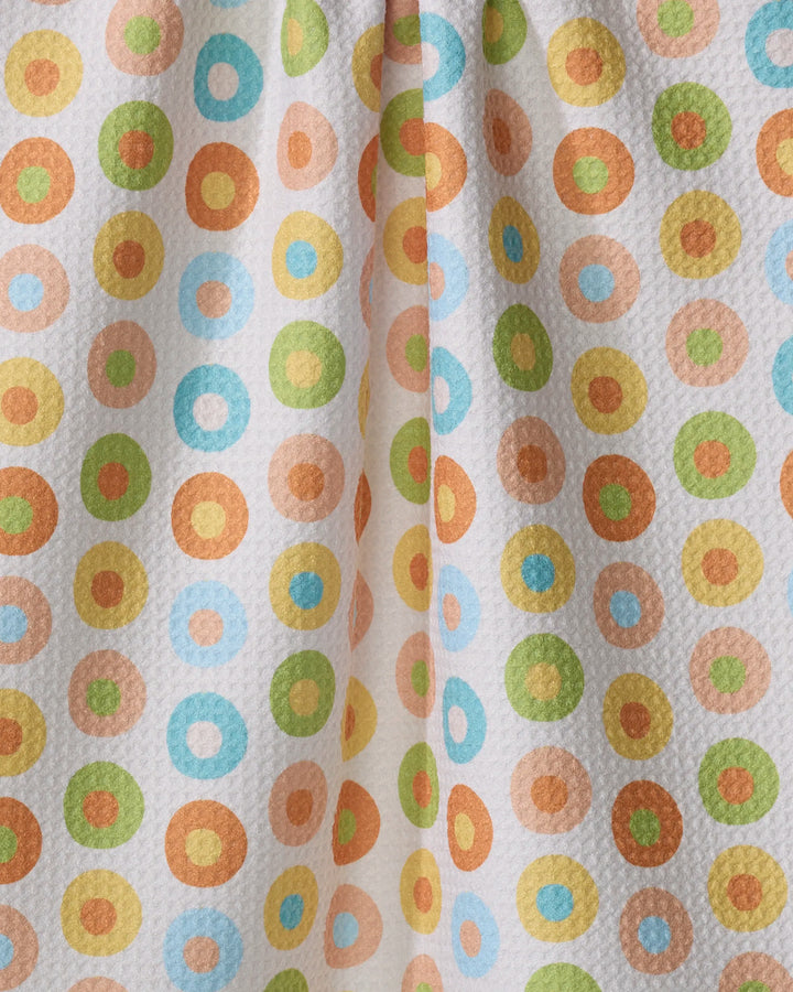 The Mindfulnice Candy Dots tea towel features a vibrant, repeating pattern of orange, green, blue, and yellow circles on textured white fabric made from recycled materials with a central fold.