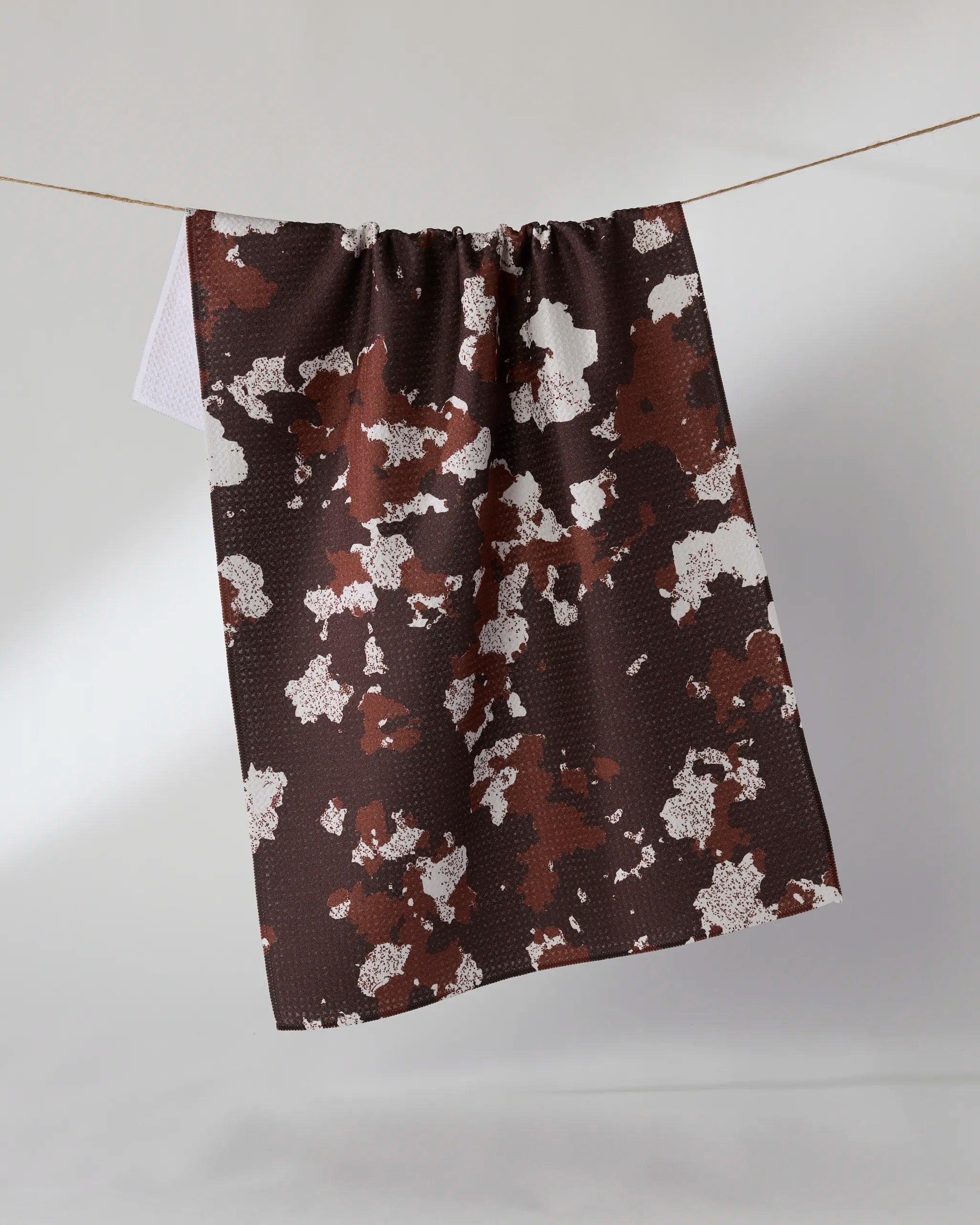 The Canyon Rose recycled kitchen towel by Geometry features a brown and white abstract pattern resembling camouflage, hanging on a string against a light background. Its ultra-absorbent fabric is both stylish and functional.