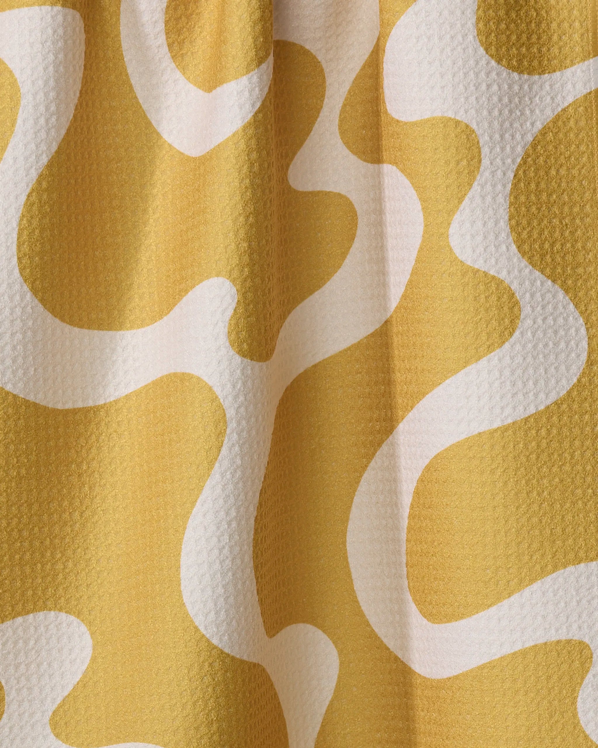 Caramel Swirl by Gerdadzy is a yellow recycled fabric with a textured surface, featuring an abstract white wavy line pattern that curves and loops across the material.