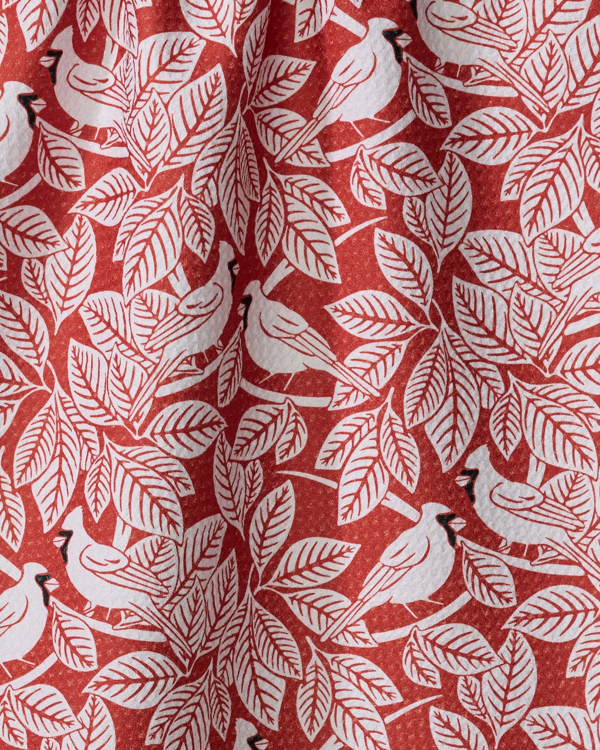 The Cardinal Canopy by Sarah Daugherty is a red recycled fabric tea towel with white stylized birds and leafy branches, offering quick-drying performance and a harmonious, nature-inspired design.