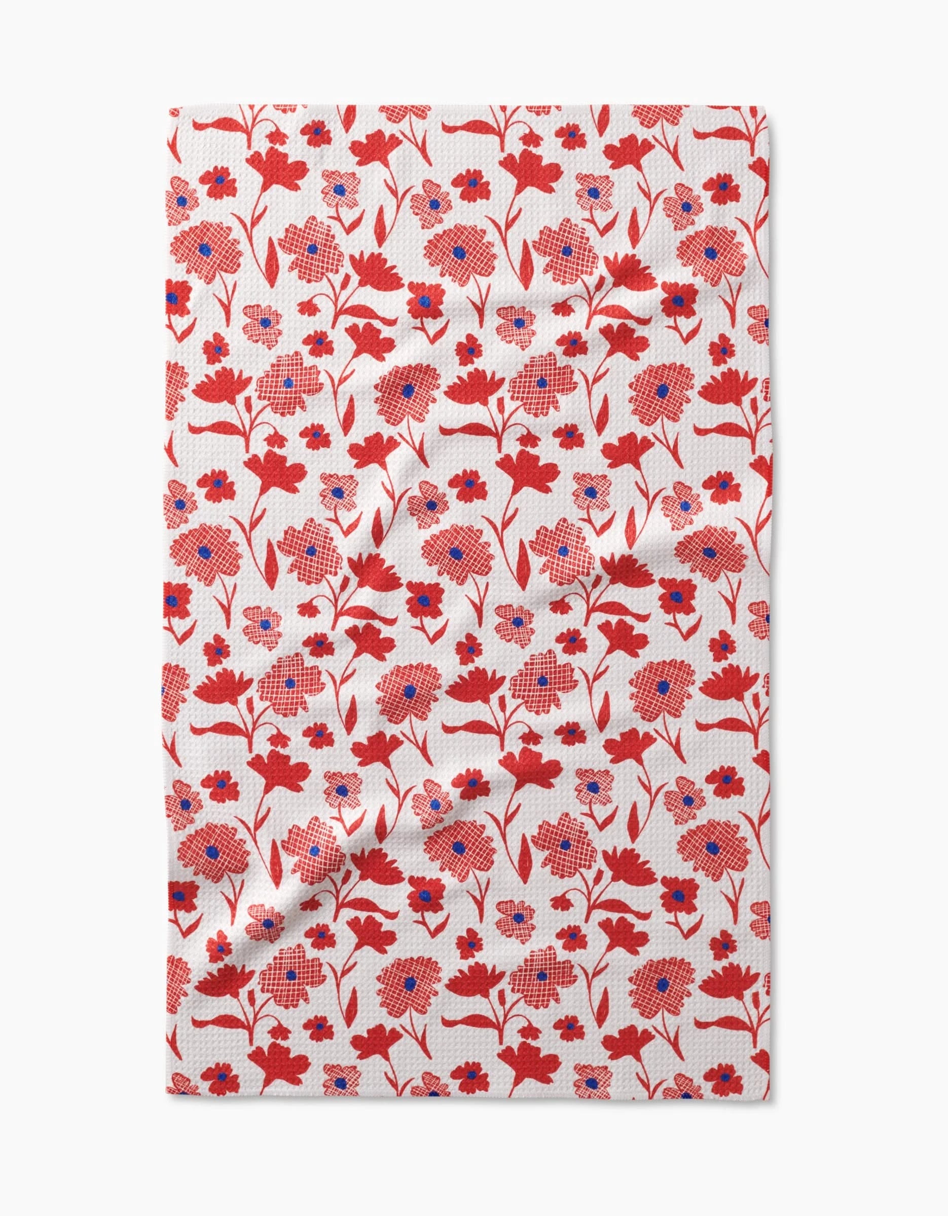 The Carmine tea towel by Danelys Sidron features a dense pattern of red and blue flowers with red stems on a white Geoweave fabric, covering the entire cloth for a vibrant, modern look.