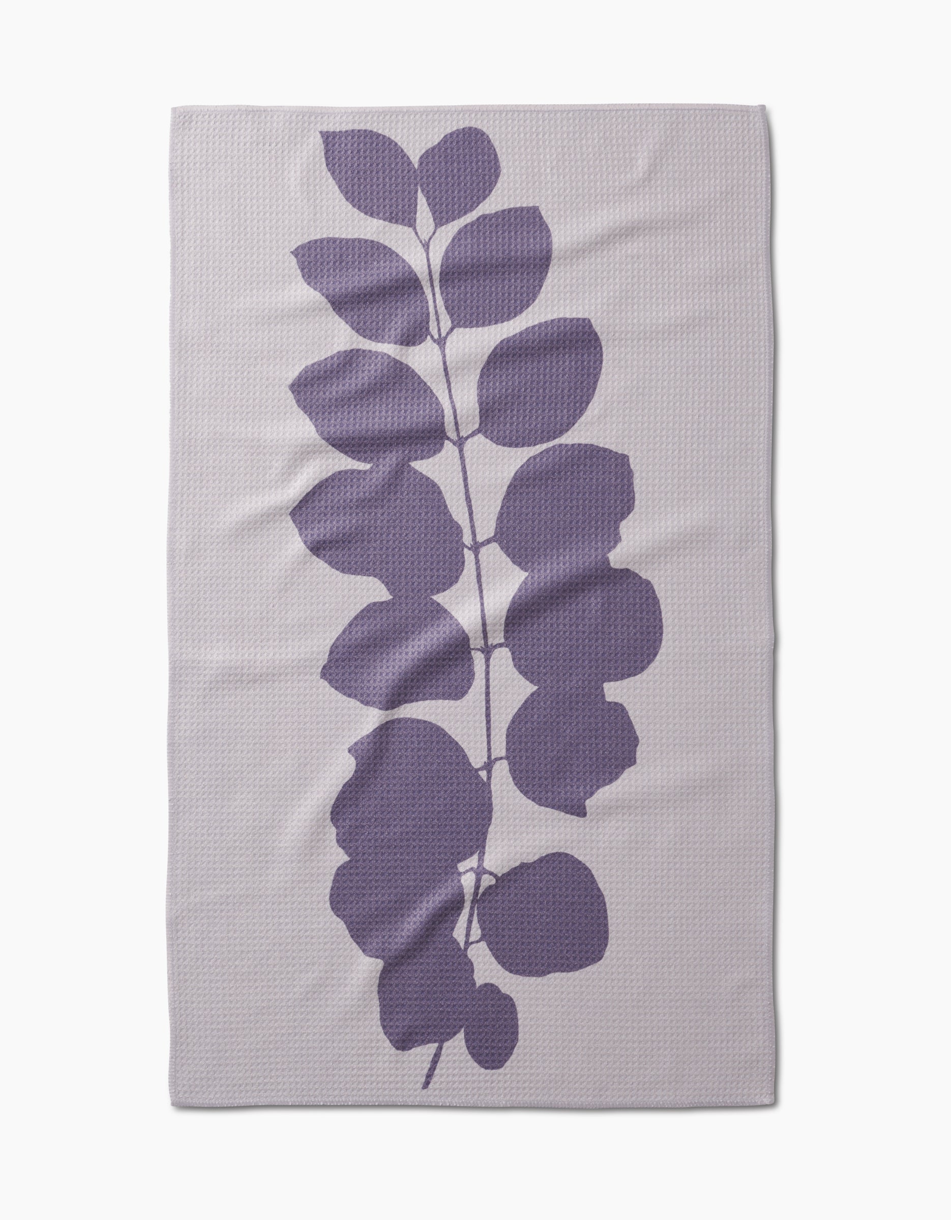 The PrintedPlant Carob blanket is light gray, rectangular, and made from ultra-absorbent Geoweave fabric. It features a large central purple leafy branch with rounded leaves on a subtly textured background.