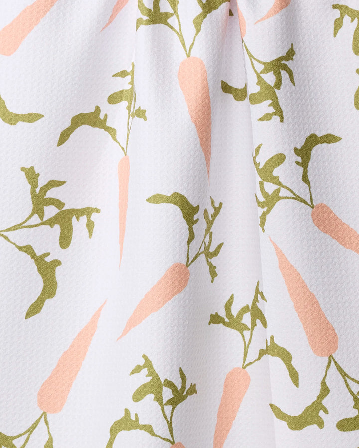 The "Carrot Toss" kitchen towel by Geometry features a white, textured, recycled fabric with a playful pattern of light orange carrots and green tops. Ultra-absorbent and stylish, it adds a fresh touch to your kitchen.