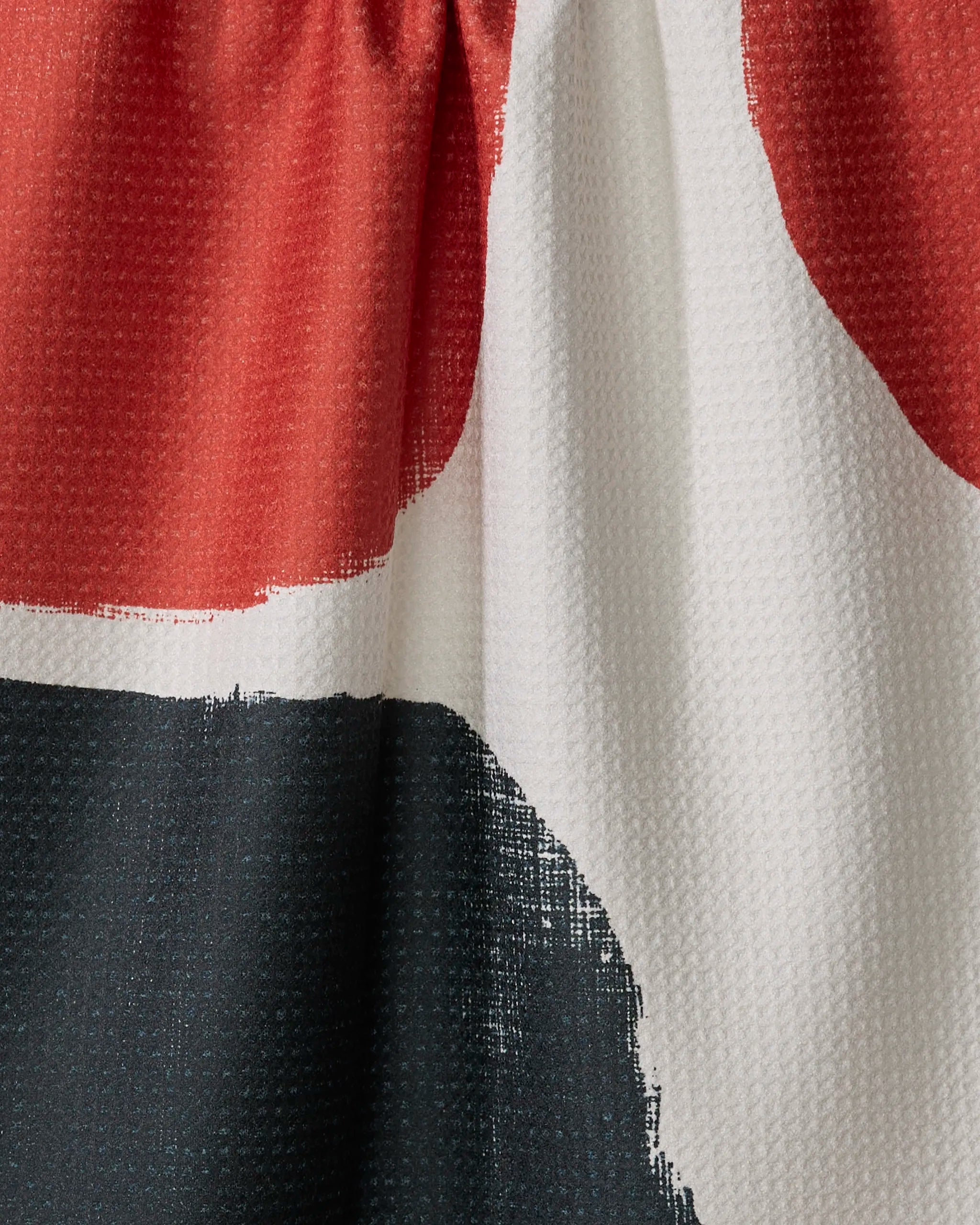 Close-up of Geometry's Cast tea towel, made from recycled materials, with visible weaves and gathered stitching at the top. Features bold, abstract color blocks in red, black, and white.