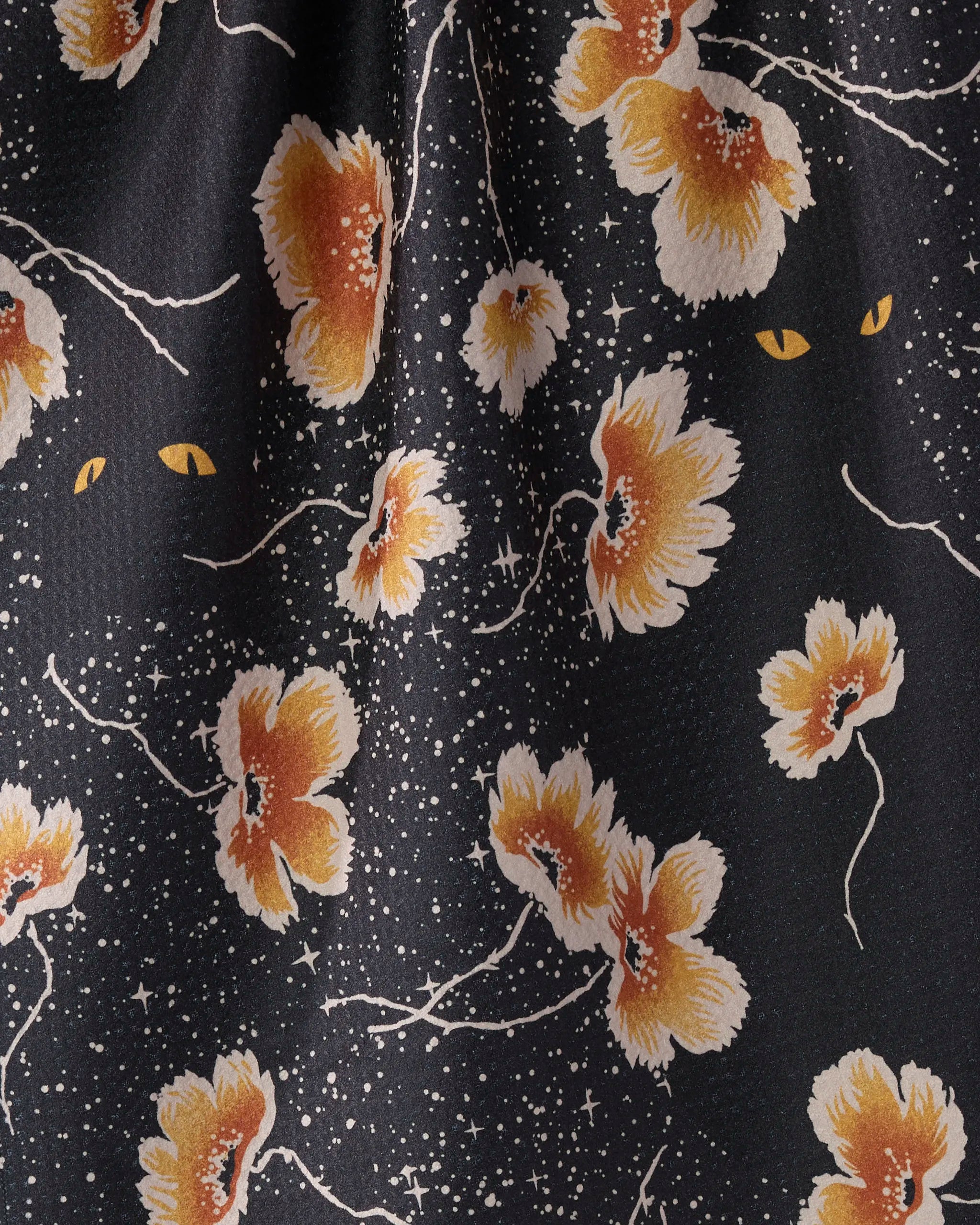 Geometry’s "Cats Eye" tea towel features large orange and white flowers, scattered star-like dots, and yellow cat eyes peeking through—crafted from recycled materials for an eco-friendly kitchen accent.
