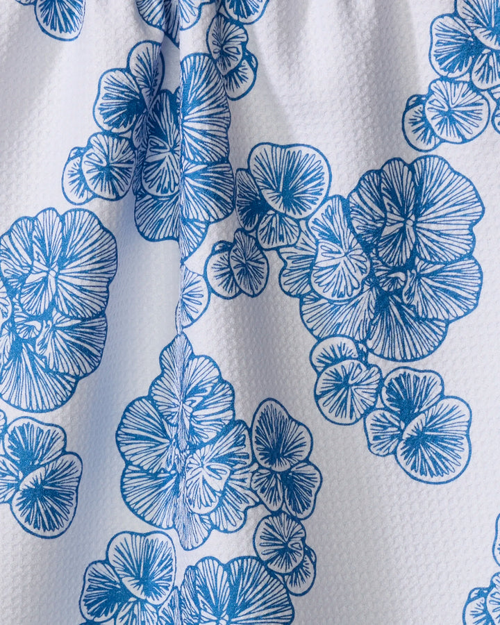 The Celia tea towel by Second Nature Studio is a white, textured kitchen towel with a blue floral pattern of stylized overlapping flowers, detailed line work, and a vertical fold down the center.