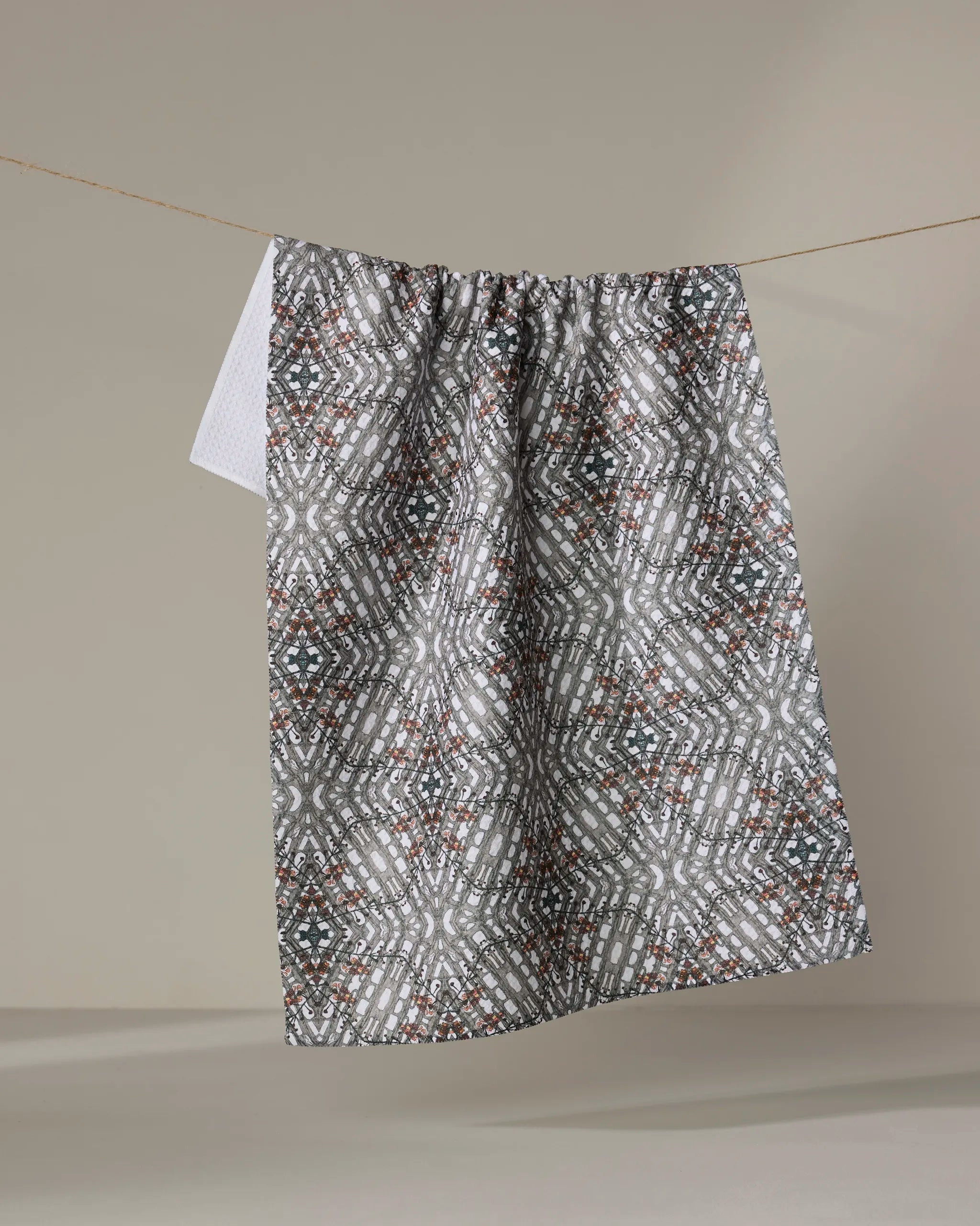 The Katherine Berkeley Cha Cha Interchange tea towel, featuring a quick-drying geometric design in gray, white, and brown, hangs on a clothesline against a plain beige background.