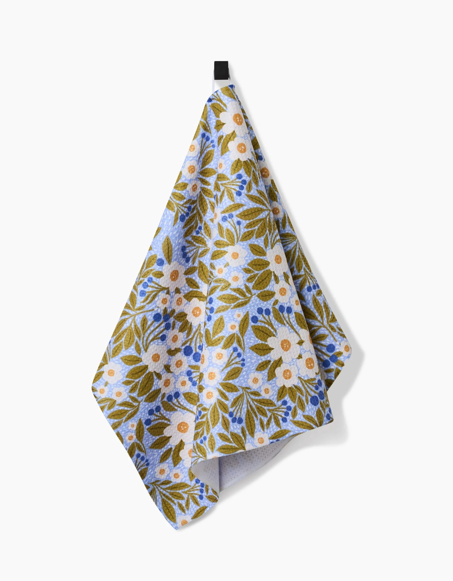 A Lisa Nelson Chamomile And Blue tea towel with blue, green, and white floral patterns hangs from a black hook. Made with durable, ultra-absorbent Geoweave™ fabric.