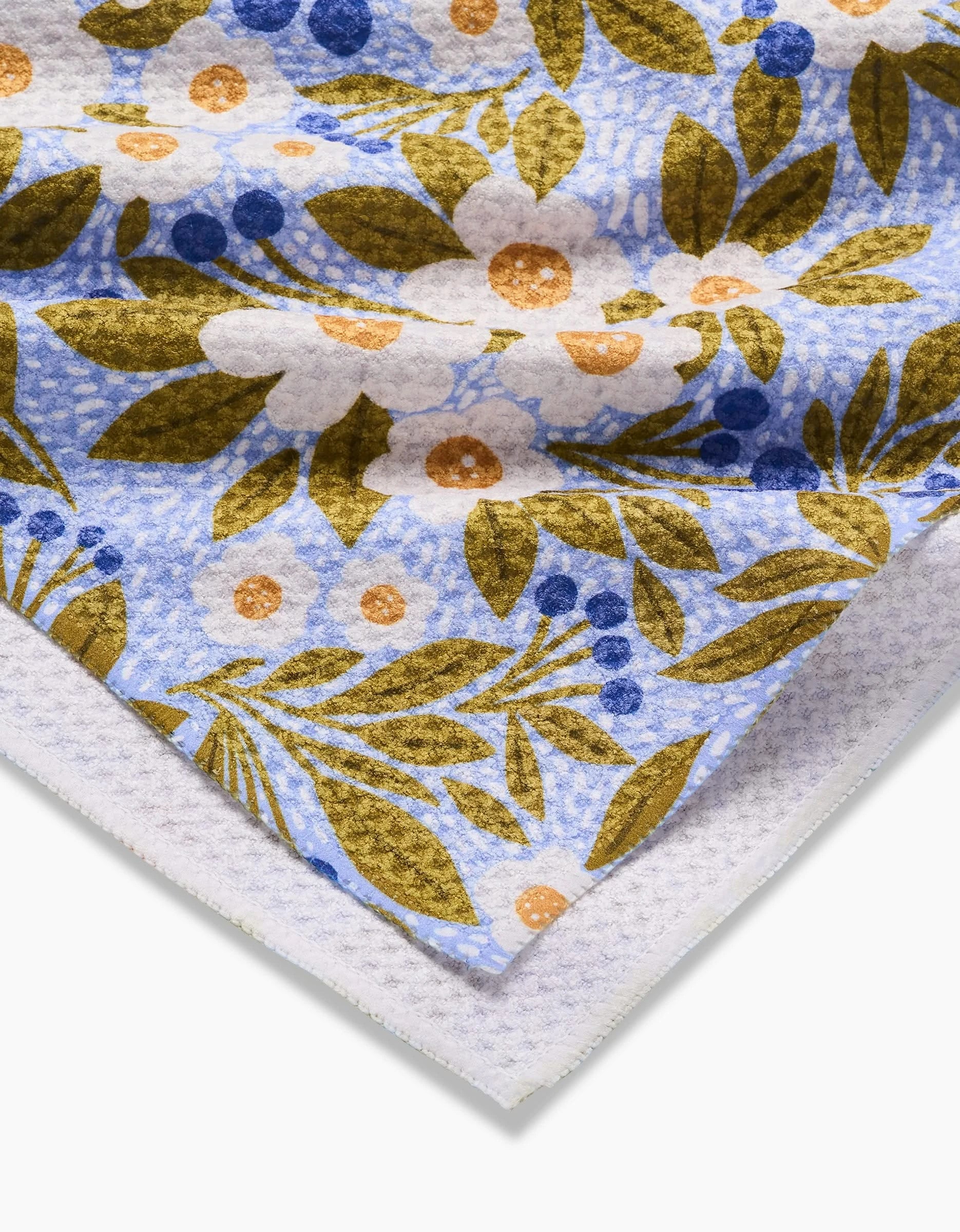 A close-up of the Lisa Nelson Chamomile And Blue Tea Towel, made from ultra-absorbent Geoweave™ fabric, featuring a floral pattern with white flowers, blue berries, and olive green leaves on a light blue textured background.