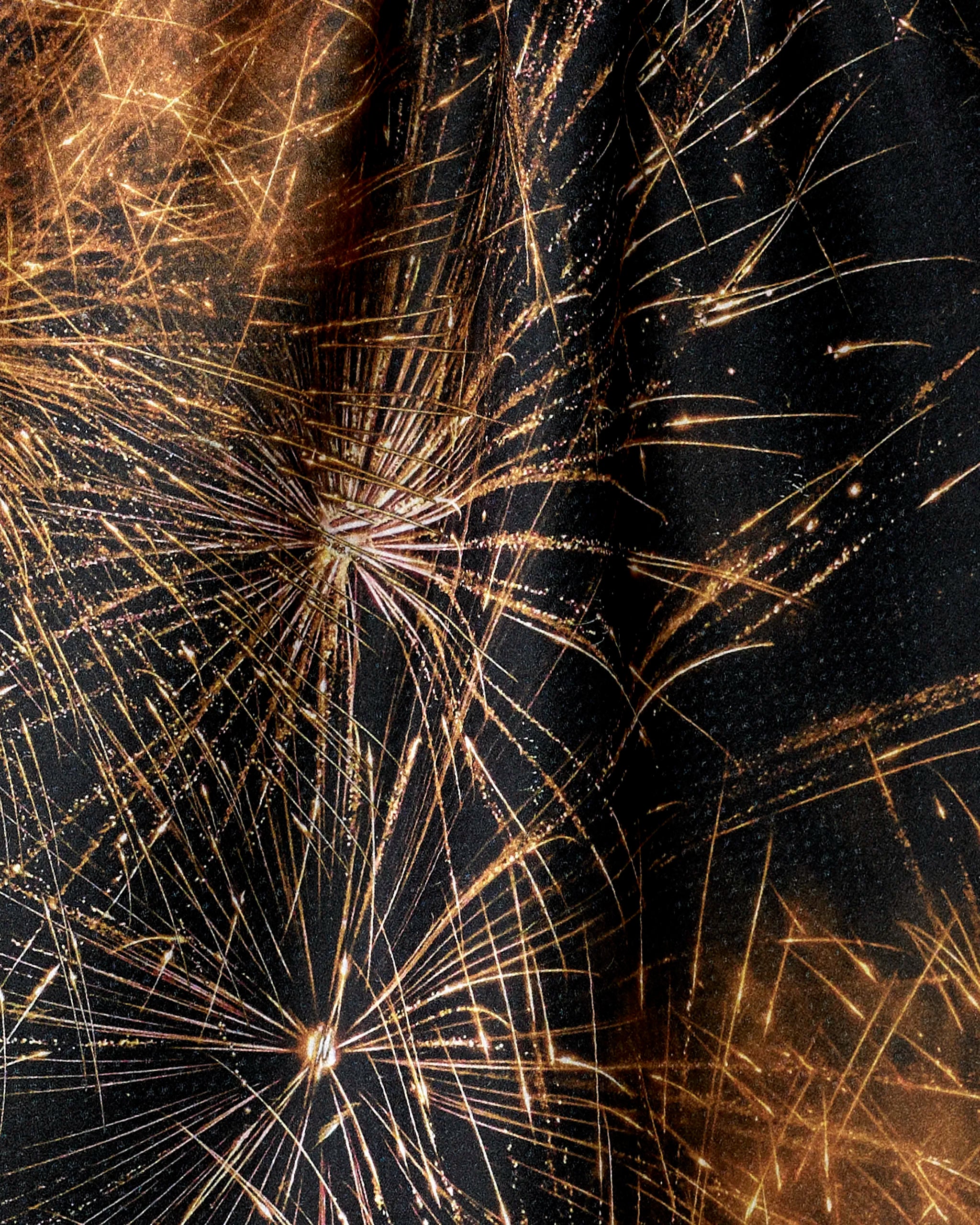 Golden fireworks burst against a dark, textured background—like radiant streaks across Geometry’s Champagne Sparkler tea towel, crafted from recycled materials—creating luminous lines of light that fan in all directions.