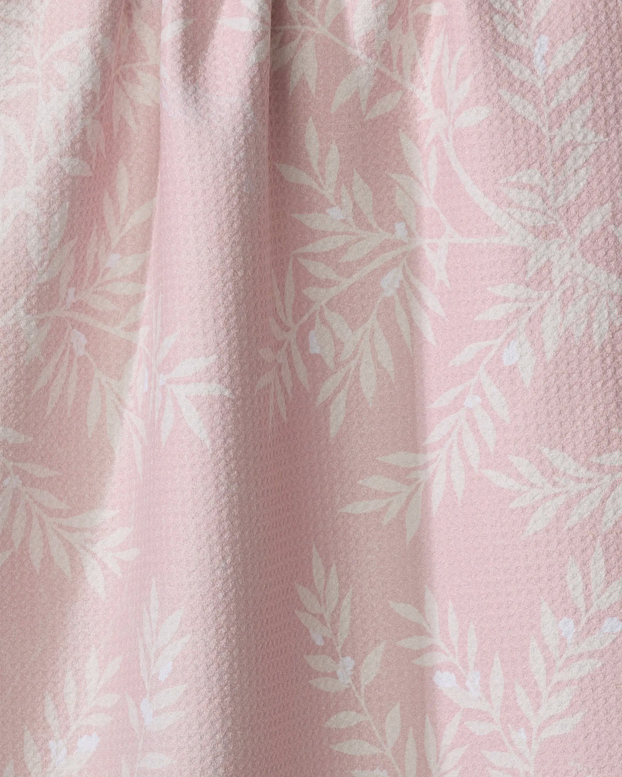 The Charlotte kitchen towel by Becki Owens showcases a light pink, recycled fabric with a white leafy branch pattern and gentle gathers, adding an elegant, eco-friendly touch to your kitchen.