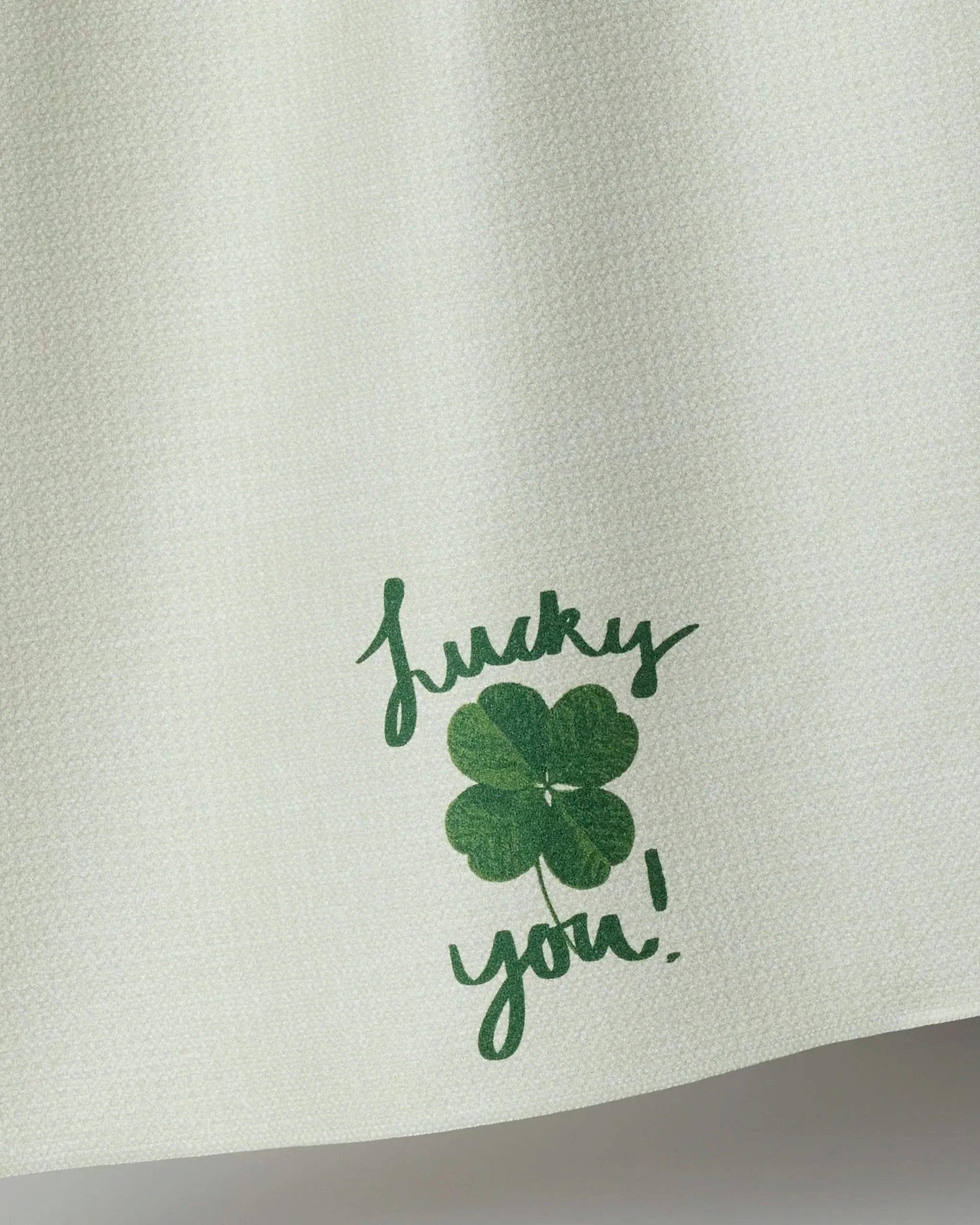 Geometry’s Charmed Up recycled kitchen towel is cream-colored and features a green four-leaf clover with the handwritten words "Lucky you!" printed below it.