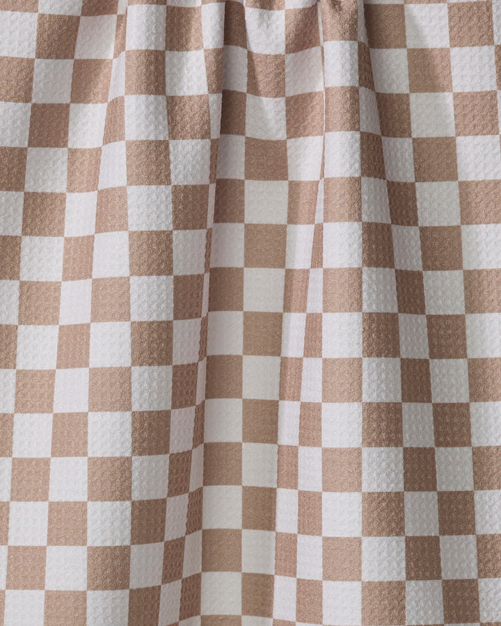 A close-up of the Check Mate tea towel by Kelsi Fullmer shows its beige and white checkered fabric with a textured surface and visible folds near the top.