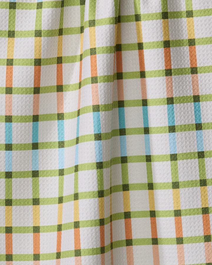 A close-up of the Mindfulnice Checkered Past tea towel shows green, orange, pink, and blue stripes on white textured Geoweave fabric. Subtle folds in the material create gentle shadows.
