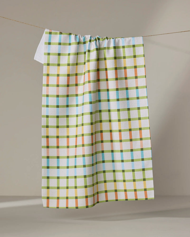 The Mindfulnice "Checkered Past" tea towel features a colorful blue, green, orange, and yellow plaid on white Geoweave fabric, shown hanging against a neutral background.