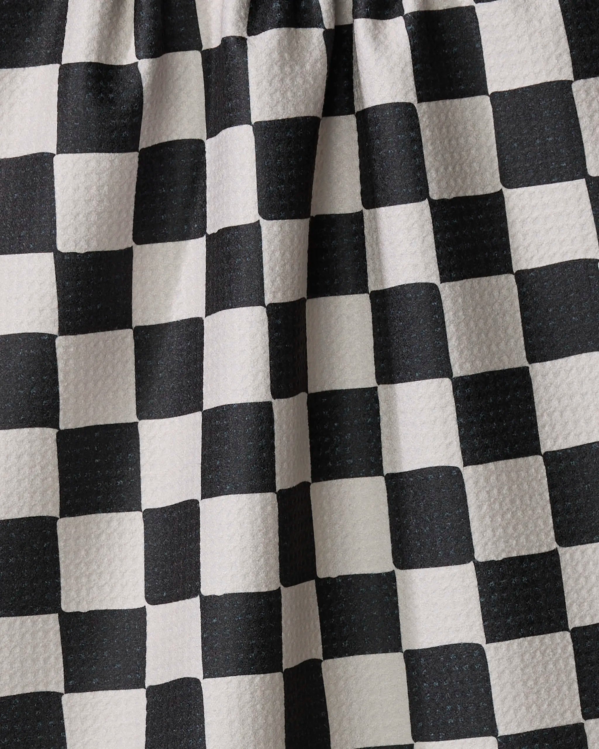 Close-up of Danelys Sidron’s Checkmate kitchen towel, featuring a black and white checkered pattern, textured surface, and gentle folds. Made from recycled materials, the fabric is arranged with gathered pleats at the top.