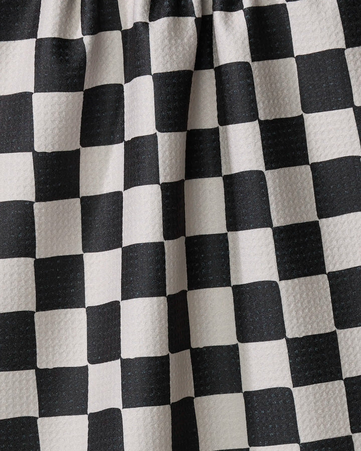 Close-up of Danelys Sidron’s Checkmate kitchen towel, featuring a black and white checkered pattern, textured surface, and gentle folds. Made from recycled materials, the fabric is arranged with gathered pleats at the top.