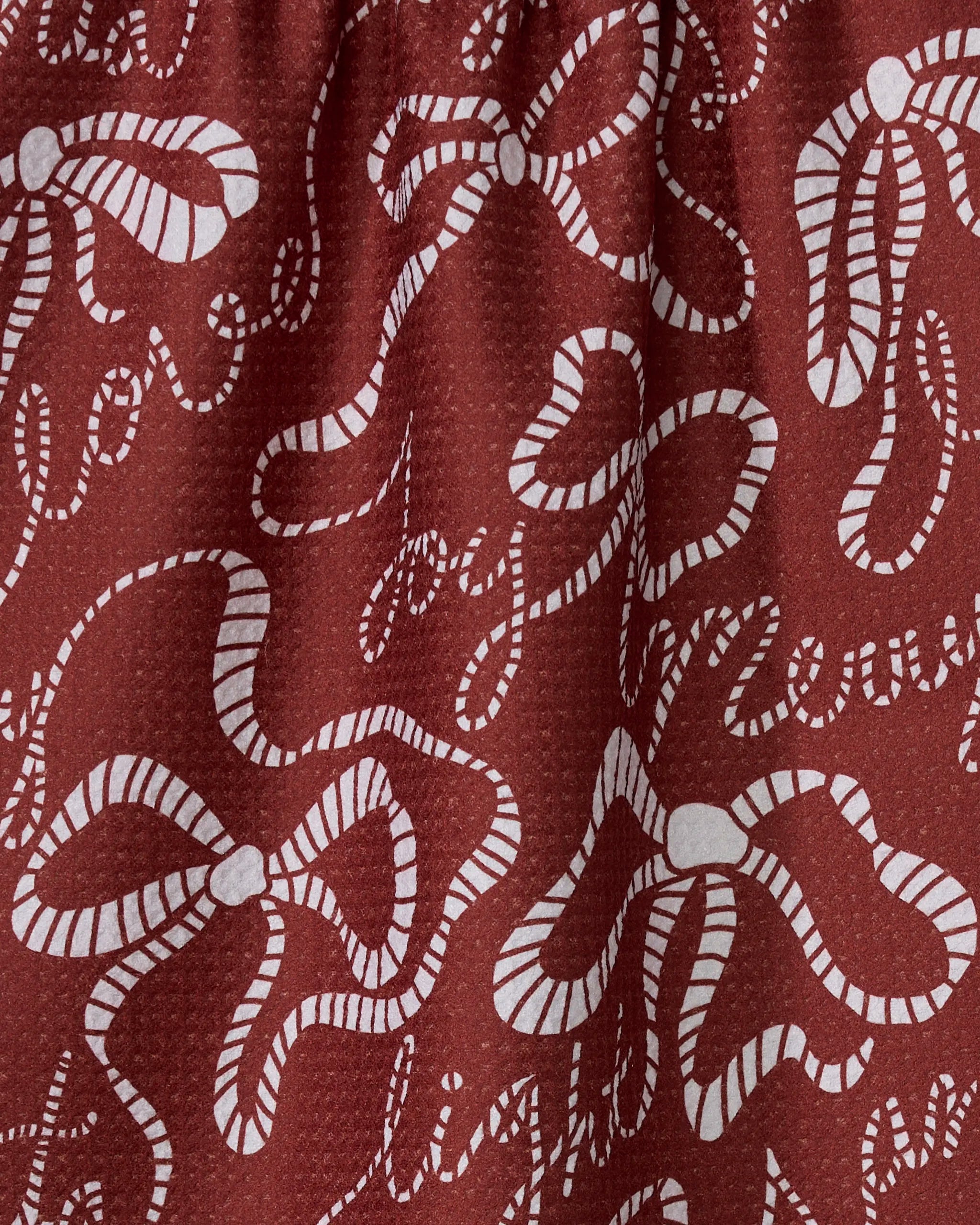 The Geometry Cheerful Bows tea towel features a brown background with white, swirling ribbon bows and cursive words like love, joy, and light. Made from recycled materials, it has a slightly textured surface.