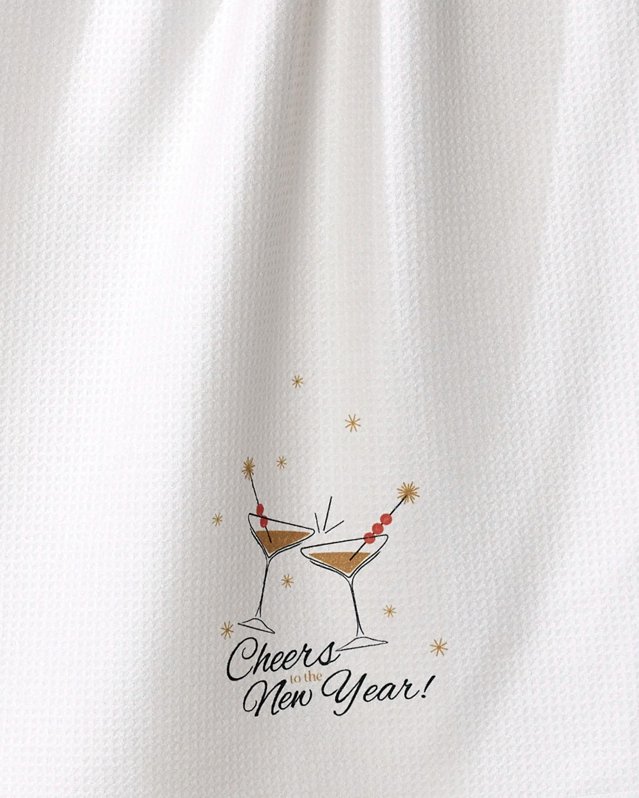 The "Cheers" tea towel by Geometry features a white textured design with two illustrated clinking cocktail glasses, gold stars, and "Cheers to the New Year!" text. Made from ultra-absorbent recycled materials.