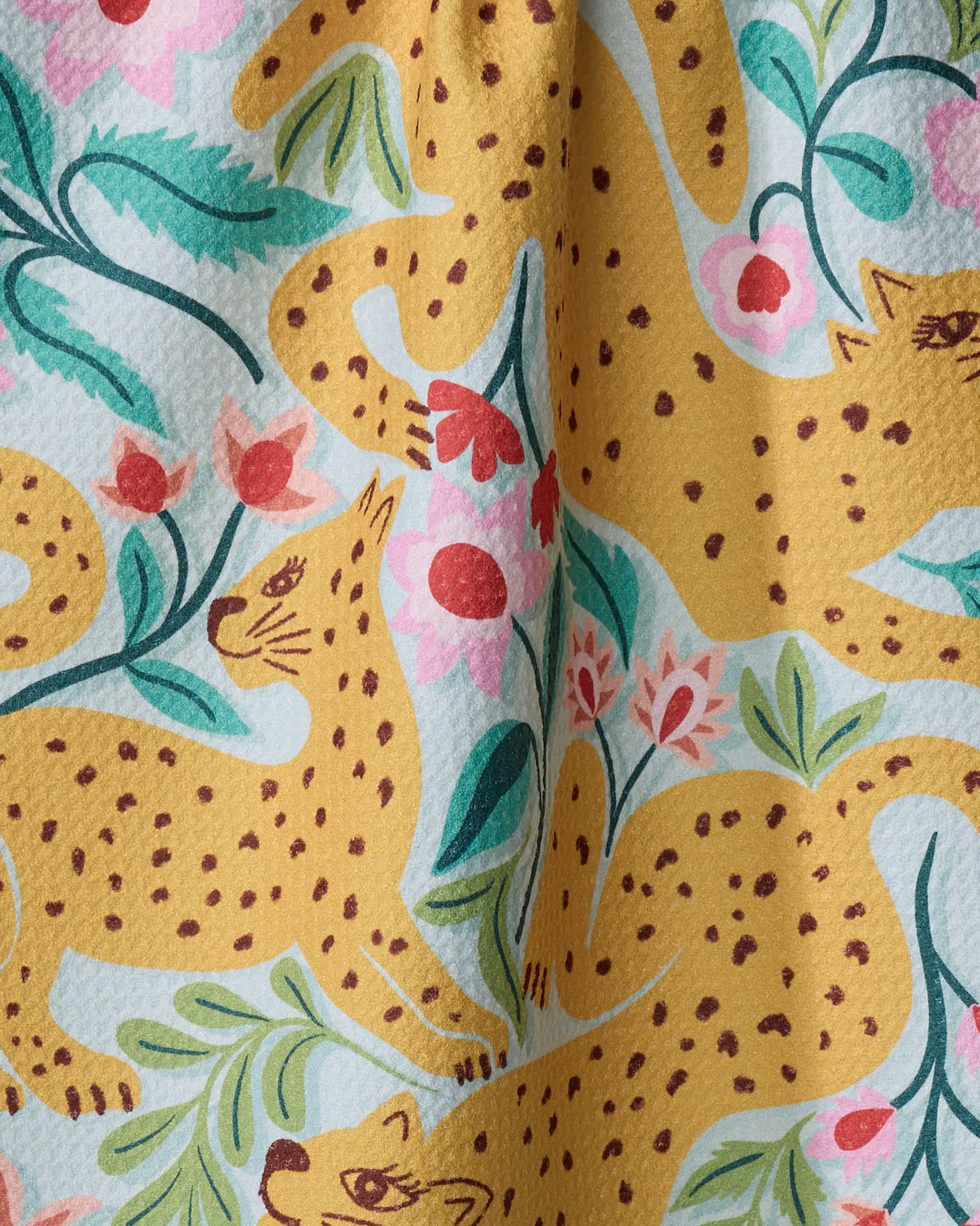 A close-up of the Cheetah Haven towel by Jasmine Blooms Designs, showcasing its ultra-absorbent texture and vibrant pattern of yellow cheetahs, green leaves, and pink flowers on a light background.
