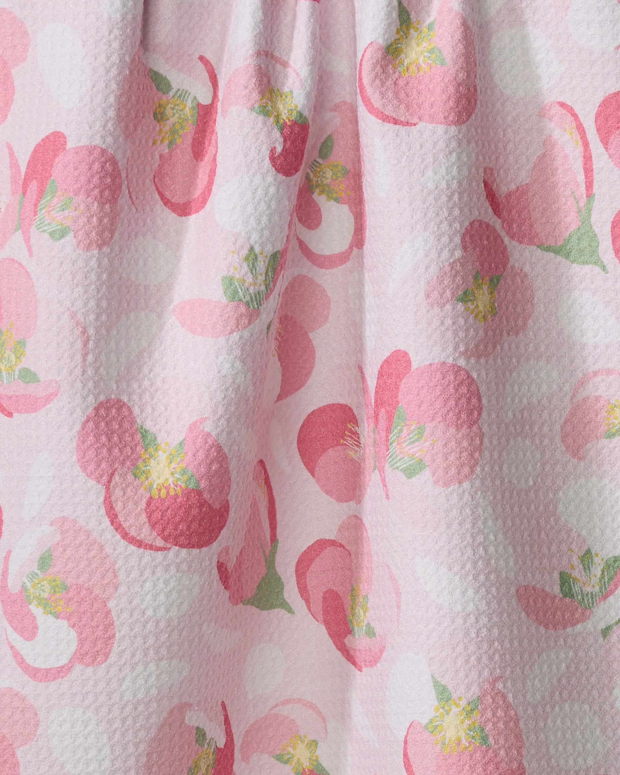 Close-up of the Cherry Blossom tea towel by Rebecca Bobko, featuring a light pink recycled fabric with large pink flowers, green and yellow centers, and subtle white polka dots.