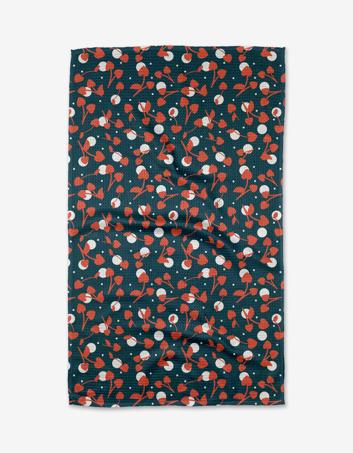 The Cherry Love tea towel by Charlie Rowan Designs features a playful pattern of red and white cherries with green stems on a dark Geoweave fabric background, arranged randomly across its rectangular surface.