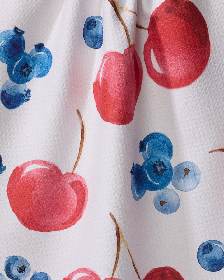 Close-up of Elena Fay’s "Cherry On Top" tea towel, showcasing a white textured fabric with a vibrant watercolor pattern of red cherries and blue blueberries.