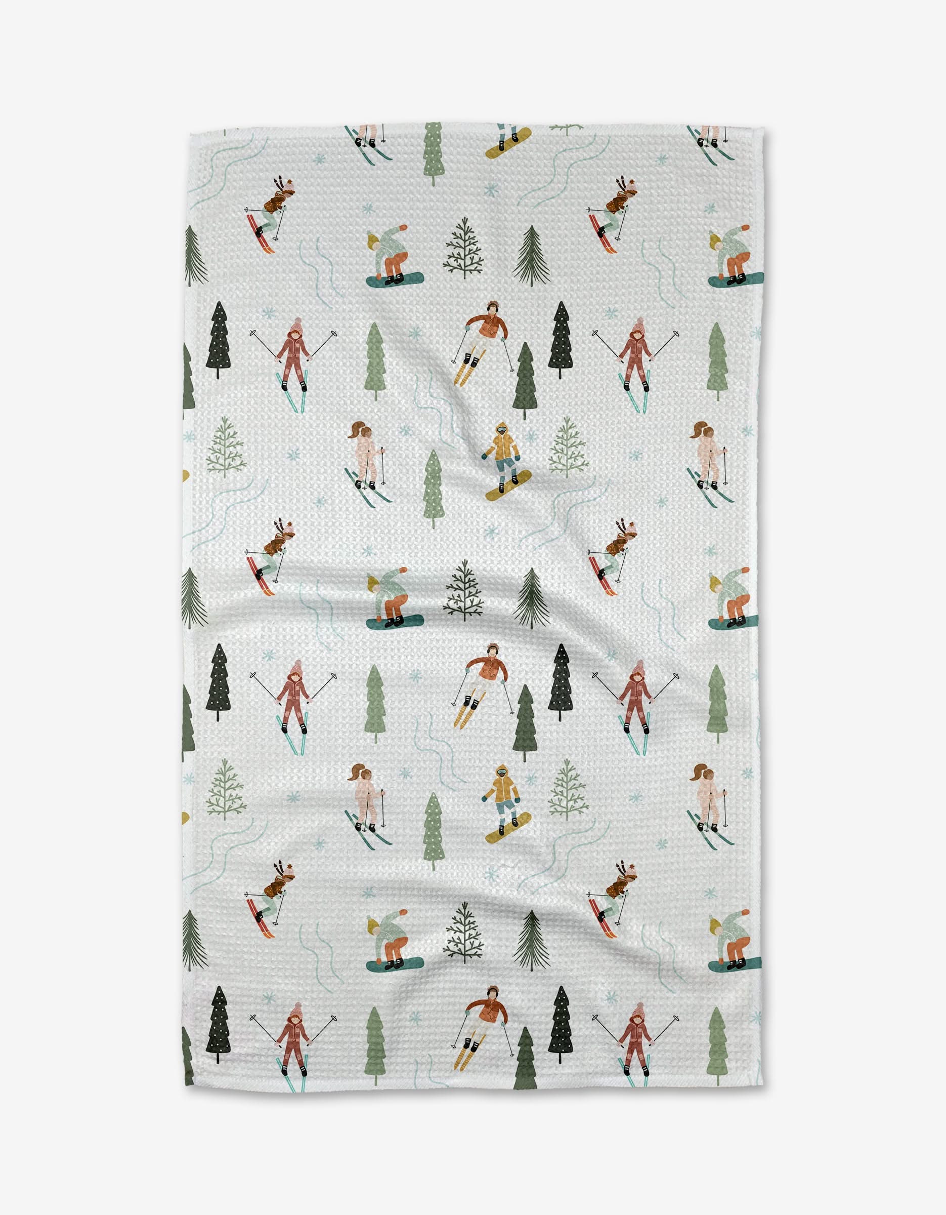 The Chill Thrill tea towel by Sara Mari features skiers in colorful outfits and evergreen trees on a snowy white background. Made from quick-drying, recycled materials, its an eco-friendly kitchen accent.