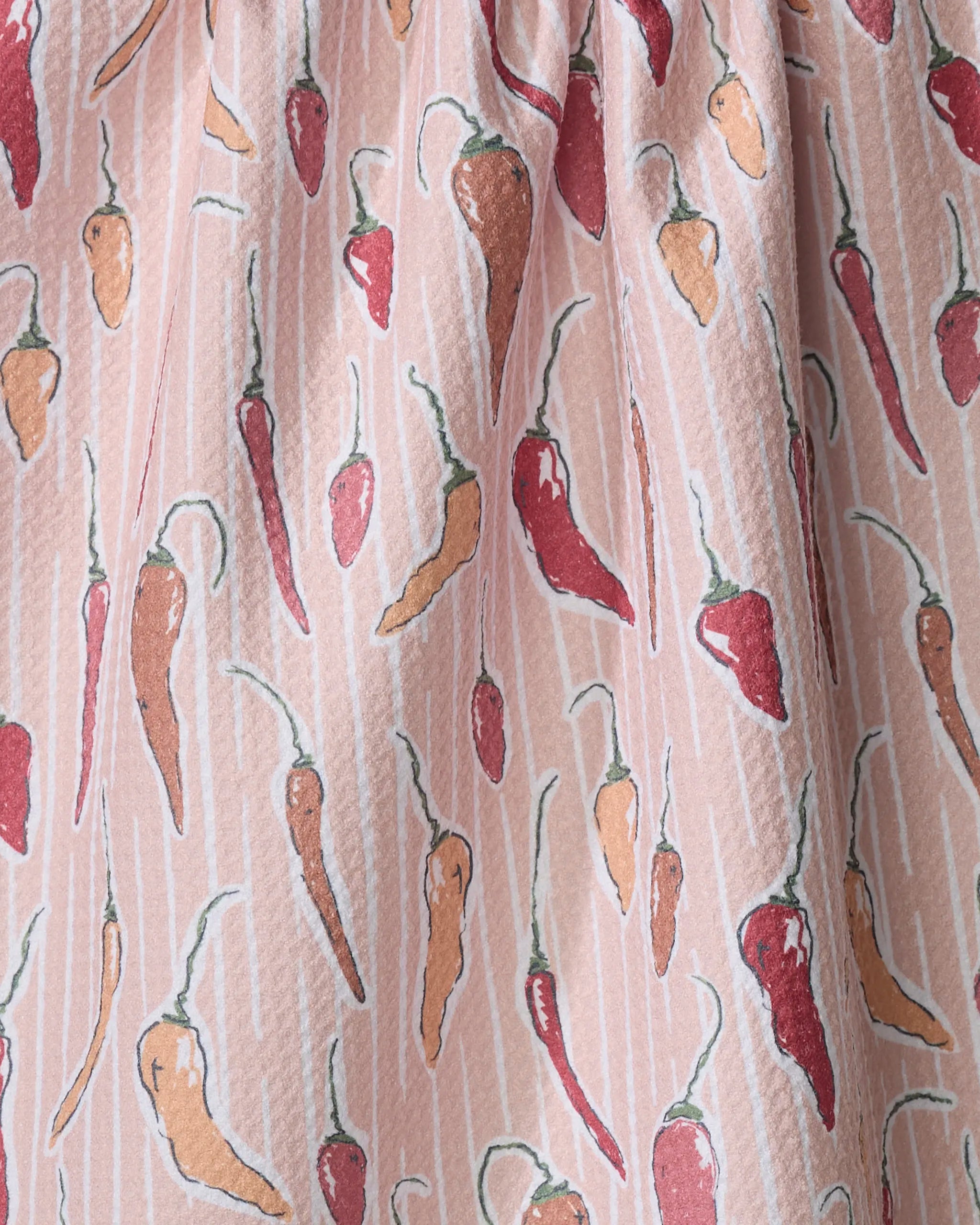 Close-up of Chilli Stripe tea towel by Hufton Studio, showcasing ultra-absorbent fabric with red and orange chili peppers on a light pink background with white stripes and green stems; material is gently gathered at the top.