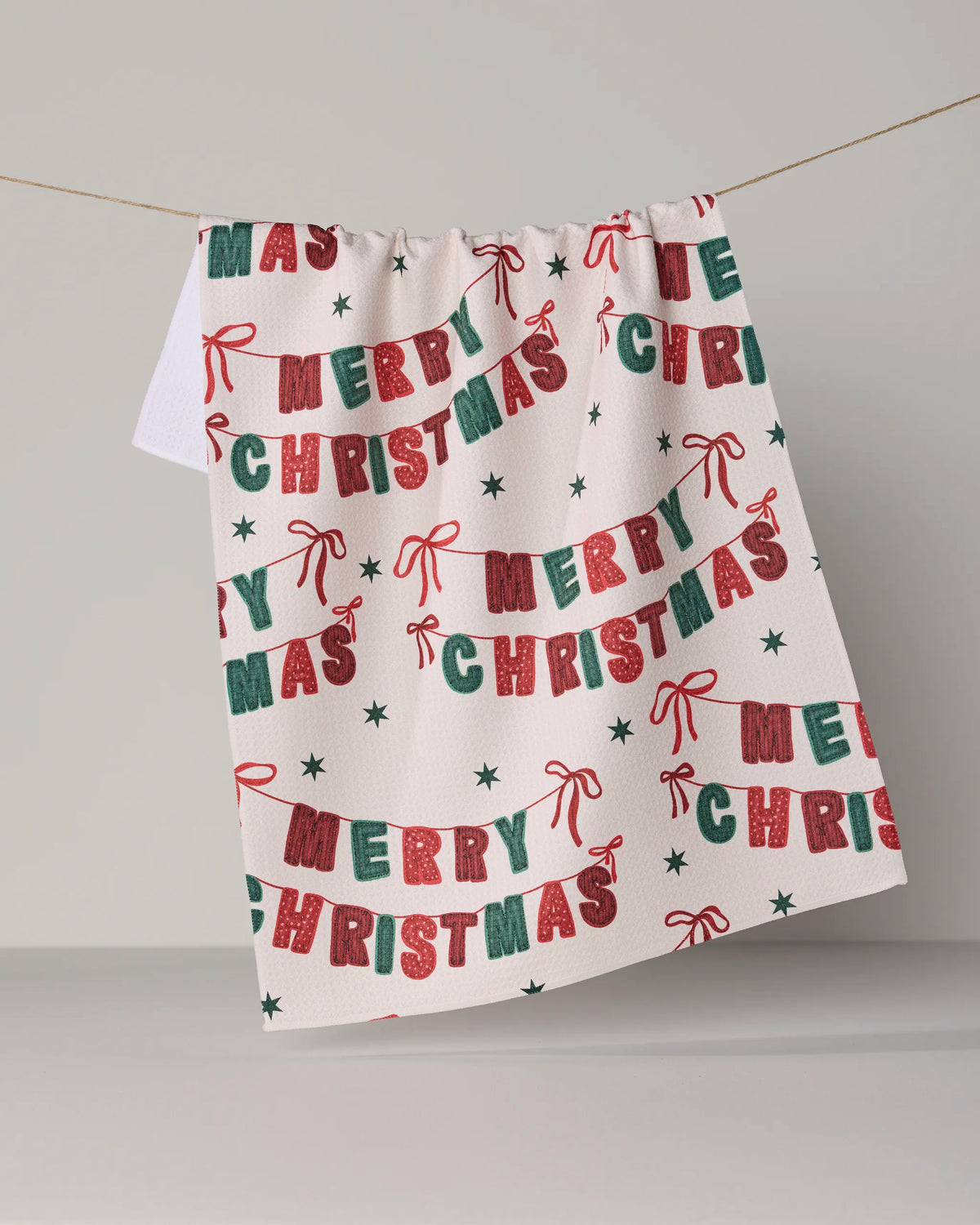 A festive Christmas Banner from Geometry hangs on a line, featuring red and green “Merry Christmas” text, small stars, and ribbon designs on a white background.