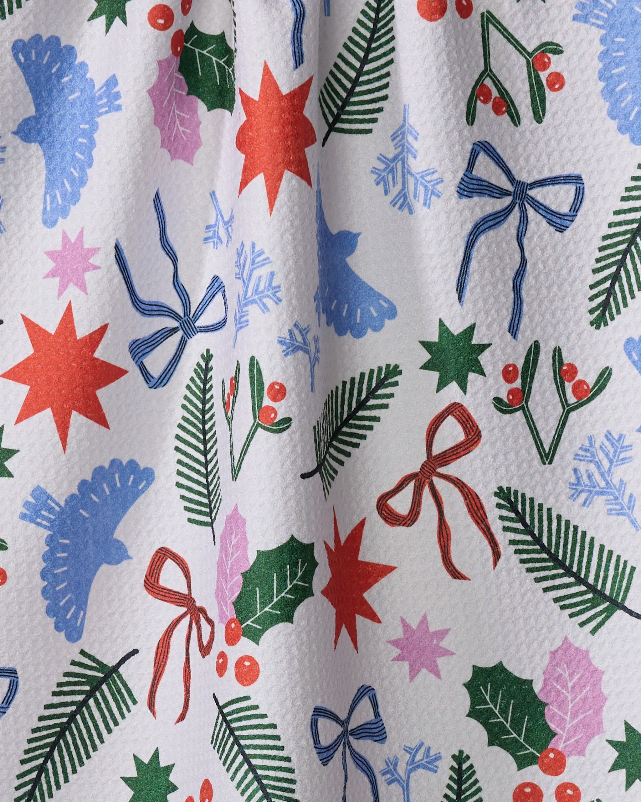 Claire Iglesias' Christmas Garden Party dish towel features blue birds, red stars, green holly leaves with berries, pine branches, blue snowflakes, and ribbon bows on textured white—festive and absorbent for your kitchen.