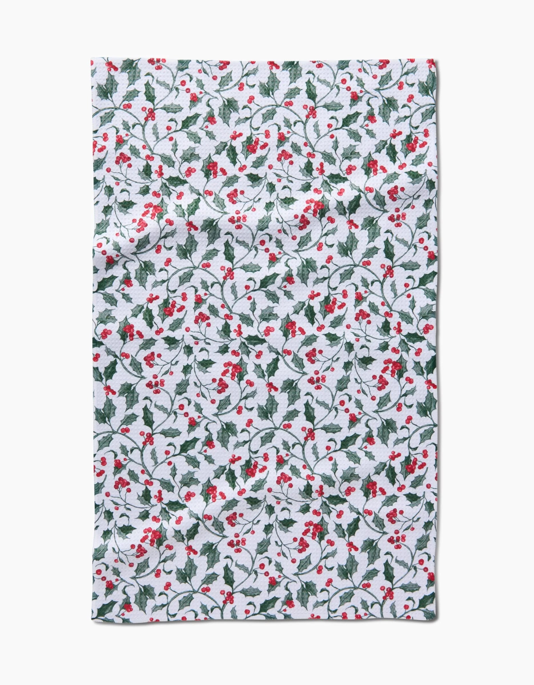 The Aubrey Fairchild Christmas Holly tea towel features a festive pattern of green holly leaves and red berries on a white background. The rectangular fabric has a slightly wrinkled appearance.