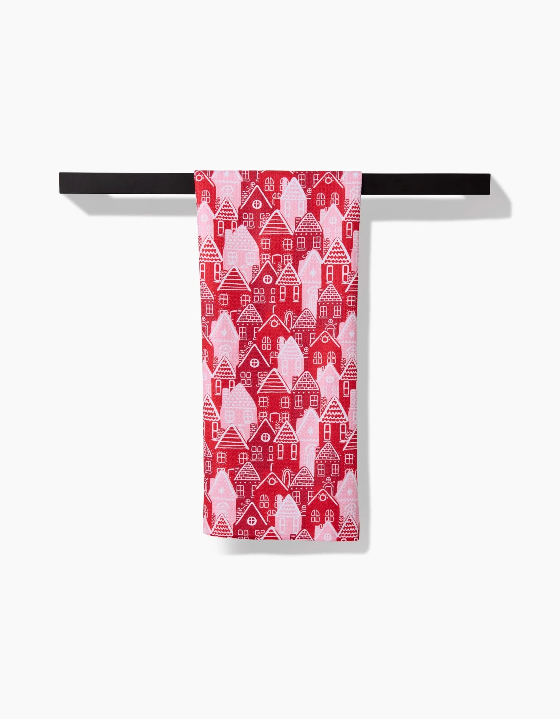 The Christmas Houses tea towel by Hufton Studio, made from recycled kitchen towel materials, features a white house pattern on red and hangs neatly on a black bar against a white background.