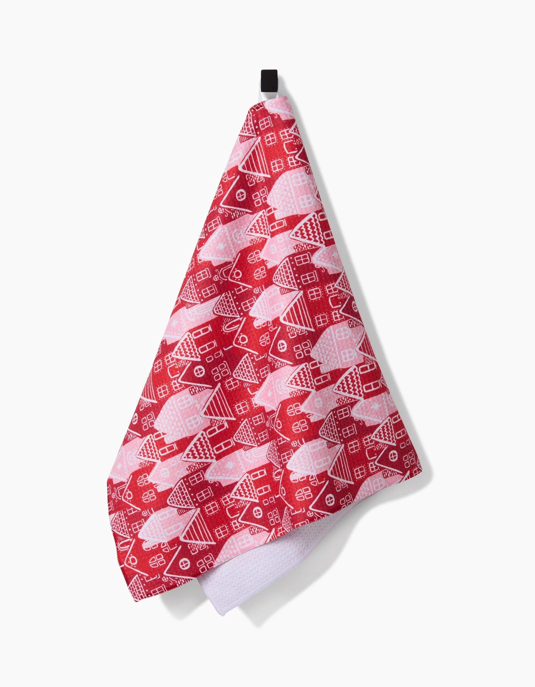 A Christmas Houses recycled kitchen towel by Hufton Studio hangs from a black hook, featuring festive red and pink patterns with white outlines of holiday houses on a vibrant background.