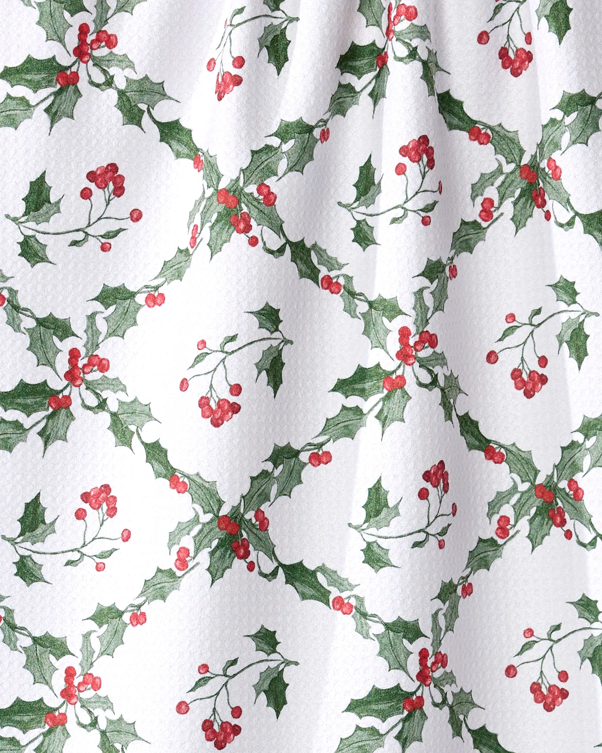 The Aubrey Fairchild Christmas Lattice kitchen towel features a white textured surface with green holly and red berry clusters in a diamond pattern for a festive holiday look. Made from recycled materials.