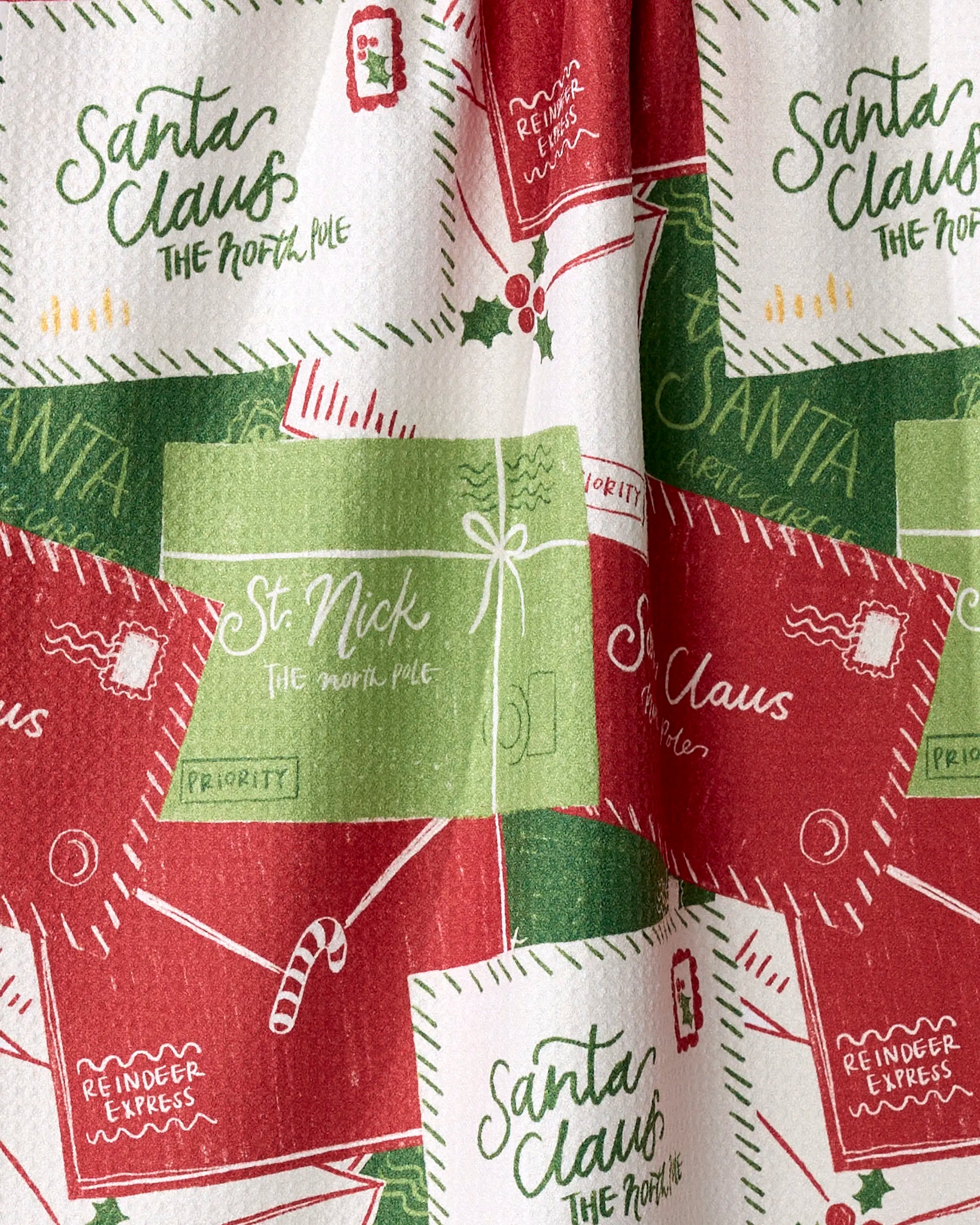 The Aubrey Fairchild "Christmas Letter Pile" tea towel features a festive pattern of red and green Santa letters, candy canes, and Reindeer Express labels—crafted from quick-drying, recycled materials.