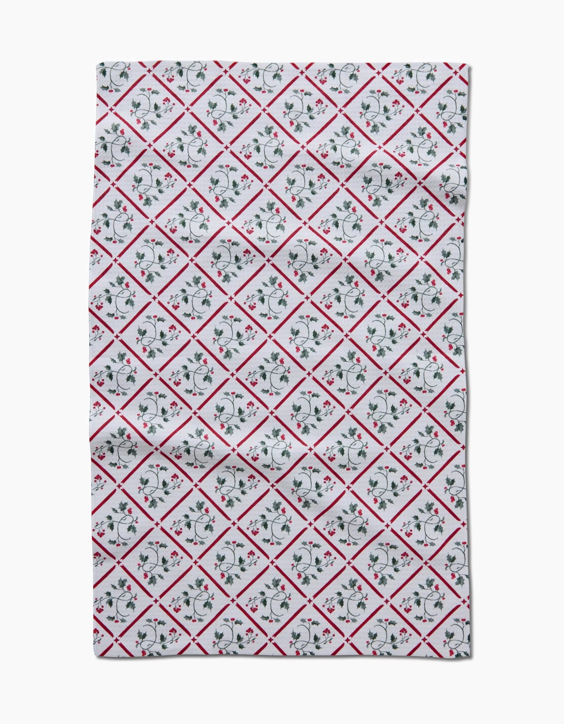 The Christmas Mistletoe Trellis tea towel by Aubrey Fairchild features a rectangular white Geoweave fabric with a diamond grid of red lines and red and green floral designs in each diamond, laid flat with slight wrinkles.
