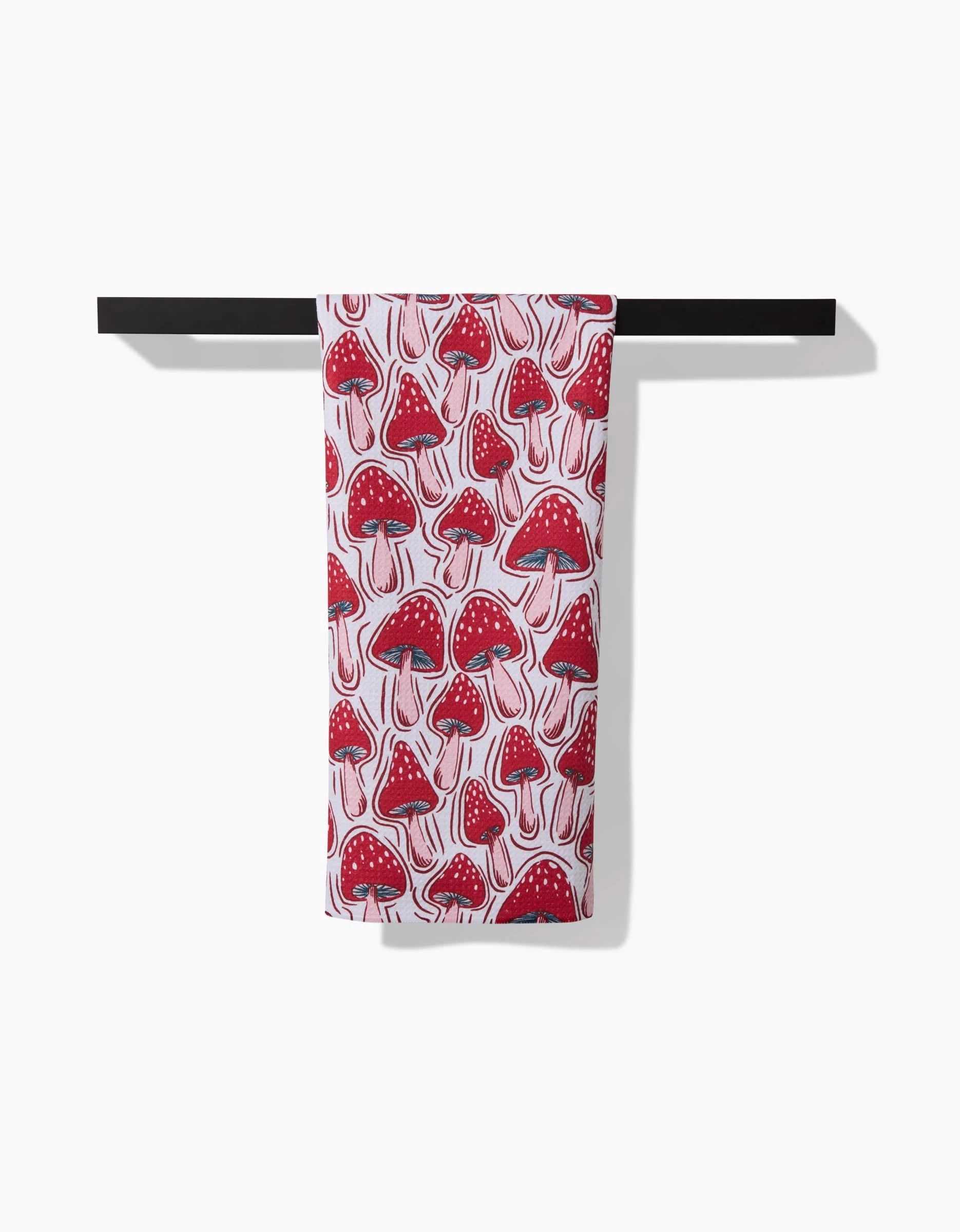 The “Christmas Mushrooms” tea towel by Hufton Studio, made from durable Geoweave fabric, displays a red and white mushroom pattern and hangs neatly folded over a black rod against a plain white background.