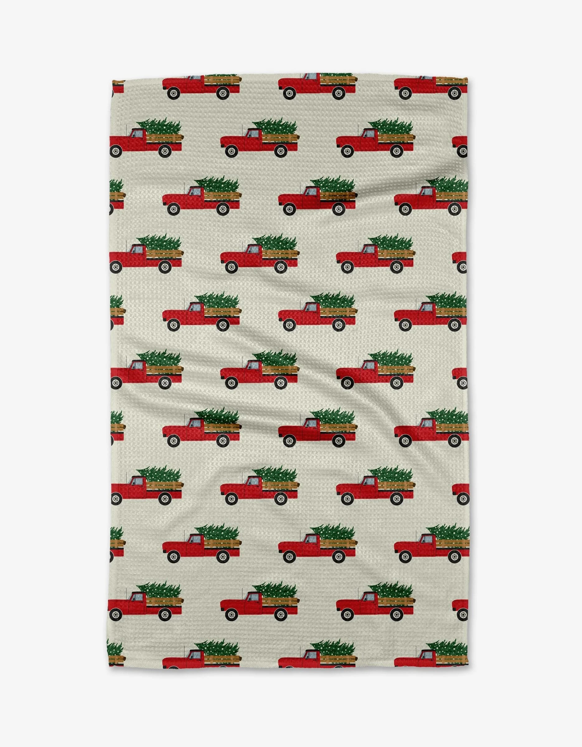 The Christmas Ride kitchen towel by Megan Kampa features red trucks with Christmas trees on a beige background and is made from recycled materials.