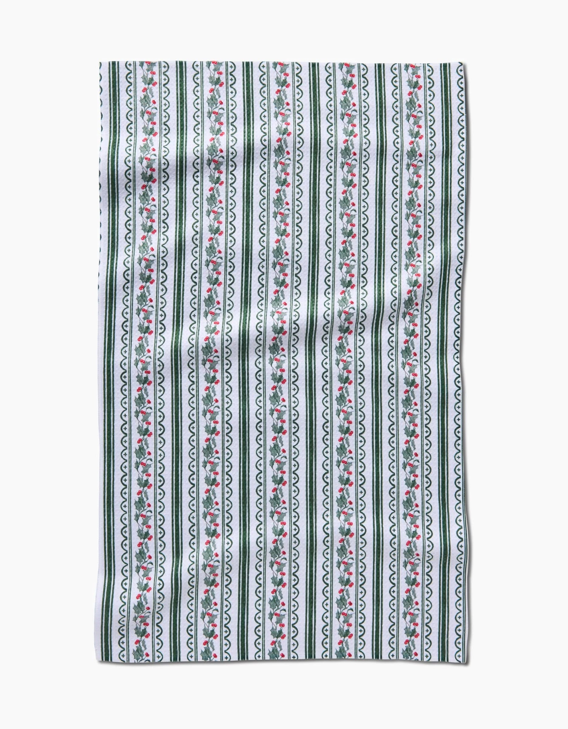The Christmas Vines tea towel by Aubrey Fairchild features vertical green stripes, black scalloped lines, and pink floral patterns on a white background with straight edges. The fabric has a slightly wrinkled look.