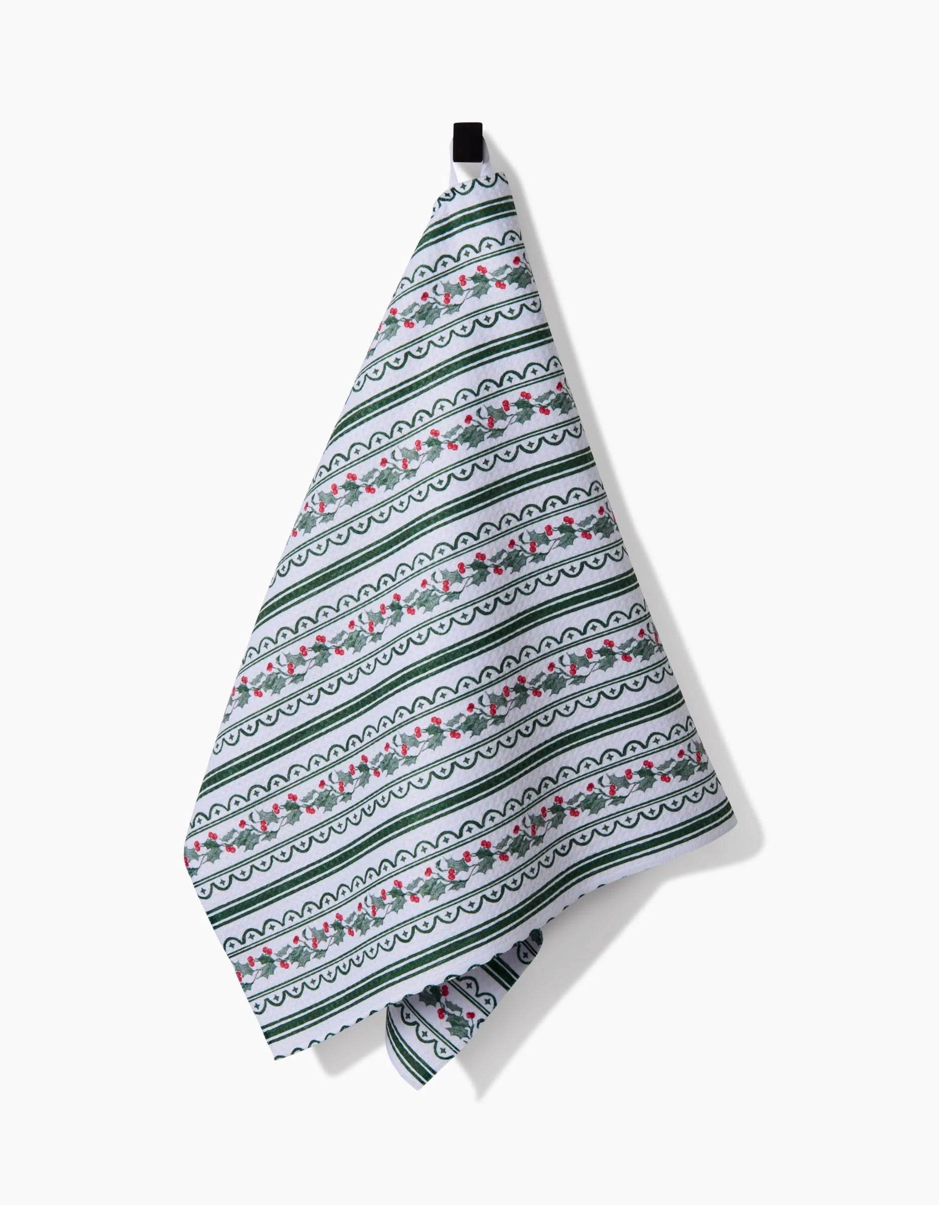 The “Christmas Vines” tea towel by Aubrey Fairchild, featuring a green, white, and pink floral stripe, hangs from a black loop against a white background—an ultra-absorbent choice for daily kitchen use.